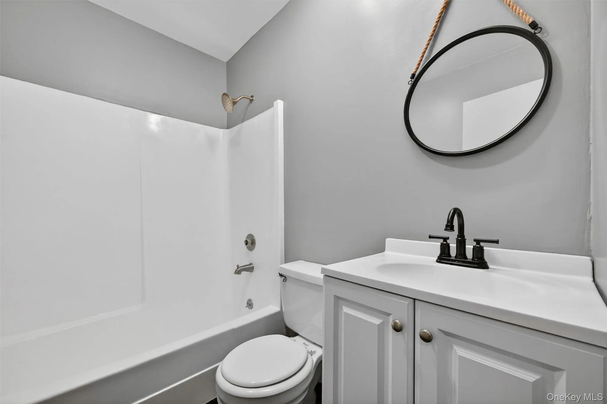 Bathroom featuring a white vanity with a single basin sink, matte black faucet, and a wall-mounted mirror Bathroom featuring a white vanity with a single basin sink, matte black faucet, and a wall-mounted mirror