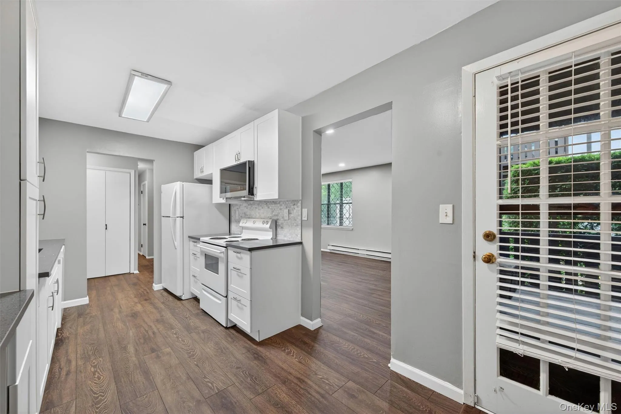 Kitchen featuring wood-finish flooring, white cabinetry with silver hardware, dark countertops, and a white tile backsplash Kitchen featuring wood-finish flooring, white cabinetry with silver hardware, dark countertops, and a white tile backsplash