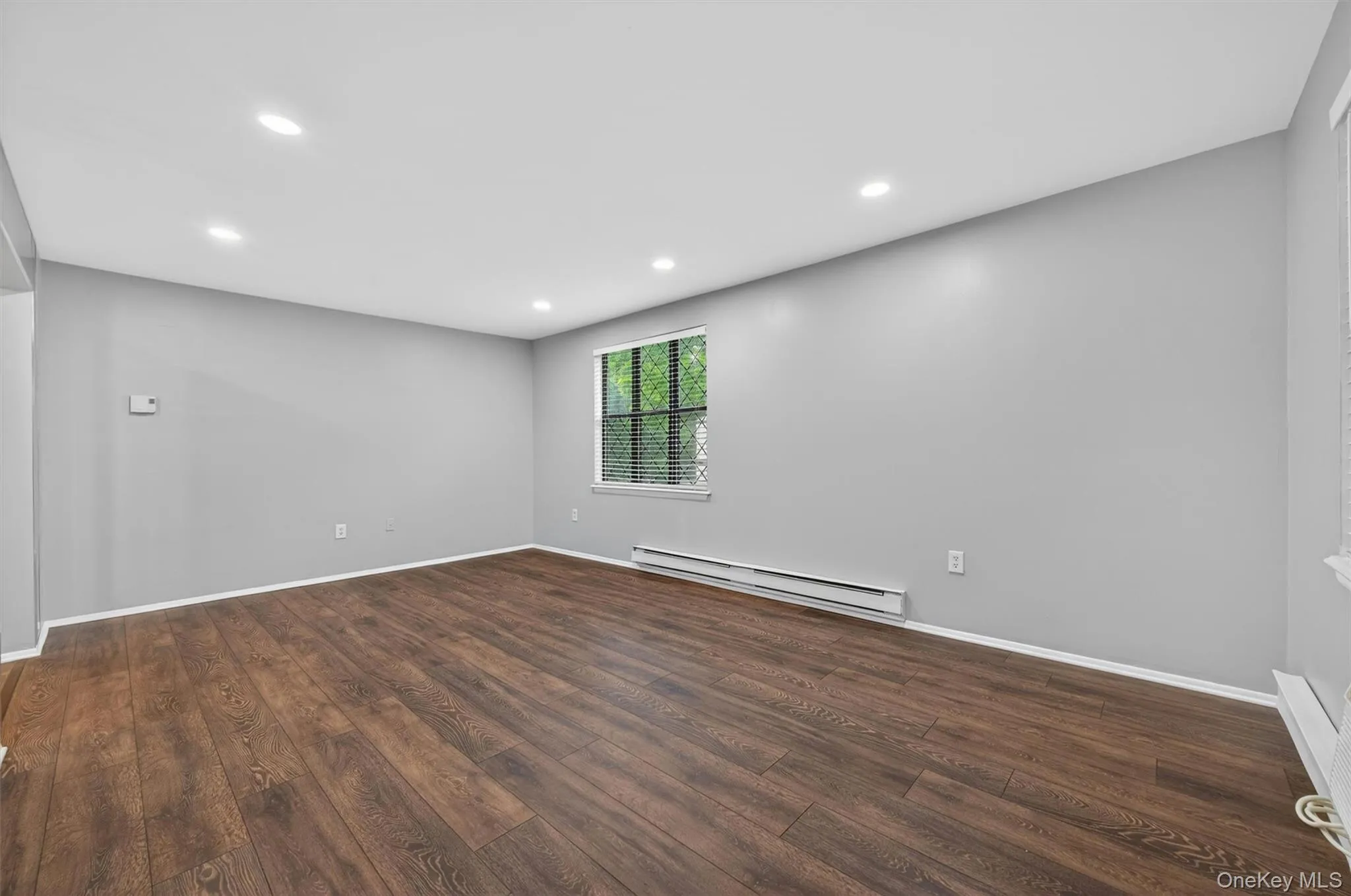 Spacious interior featuring wood-finish flooring, recessed lighting, a large window with blinds, and light gray wall finishes Spacious interior featuring wood-finish flooring, recessed lighting, a large window with blinds, and light gray wall finishes
