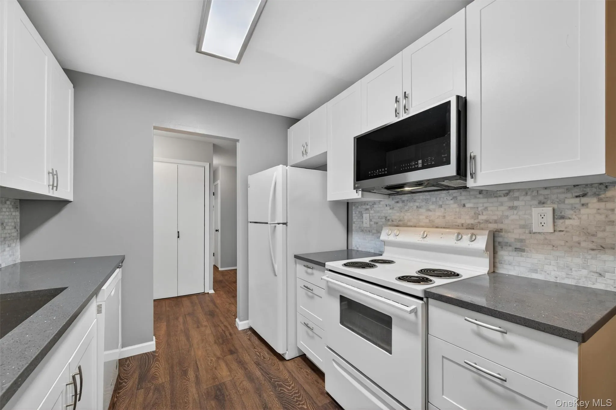 Kitchen featuring white cabinetry, dark stone-finish countertops, wood-finish flooring, a tile backsplash, and an over-the-range microwave Kitchen featuring white cabinetry, dark stone-finish countertops, wood-finish flooring, a tile backsplash, and an over-the-range microwave