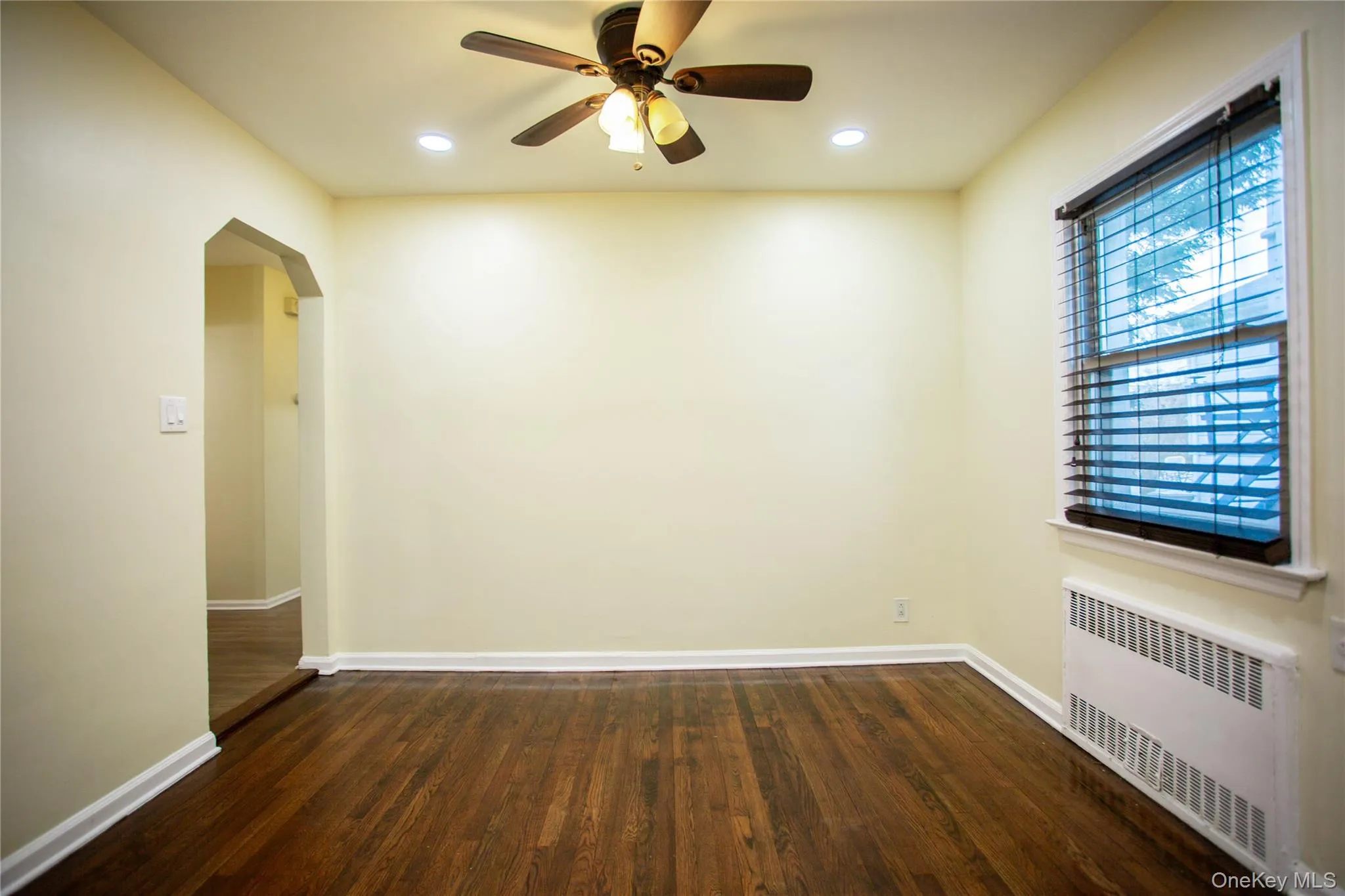 Unfurnished room featuring arched walkways, baseboards, radiator heating unit, wood finished floors, and ceiling fan Unfurnished room featuring arched walkways, baseboards, radiator heating unit, wood finished floors, and ceiling fan