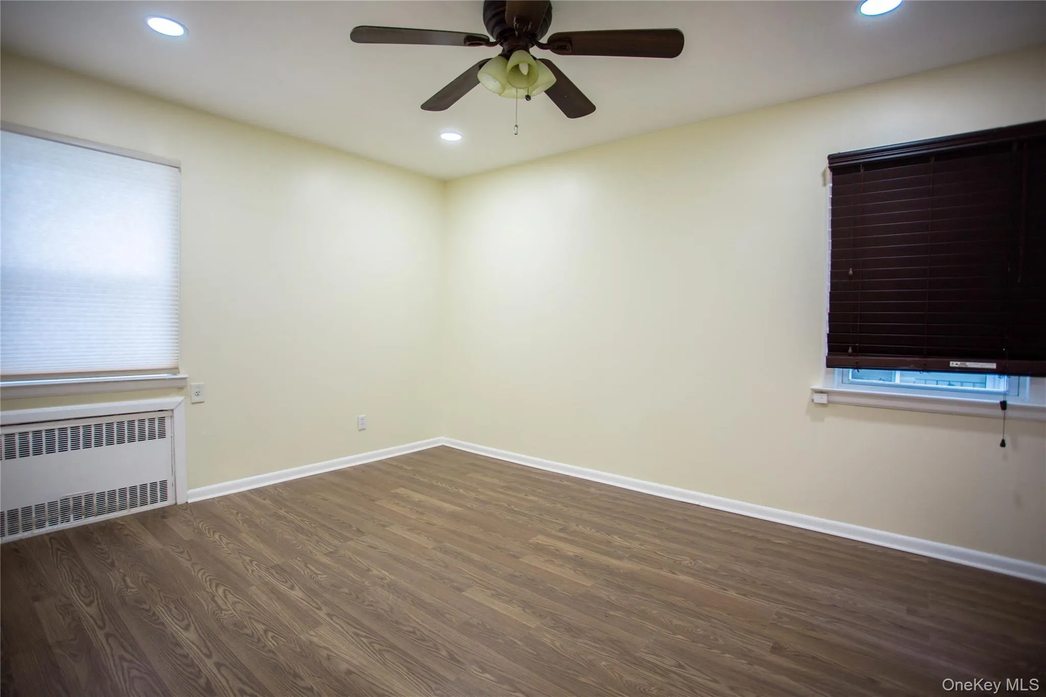 Empty room featuring recessed lighting, radiator heating unit, baseboards, and wood finished floors Empty room featuring recessed lighting, radiator heating unit, baseboards, and wood finished floors