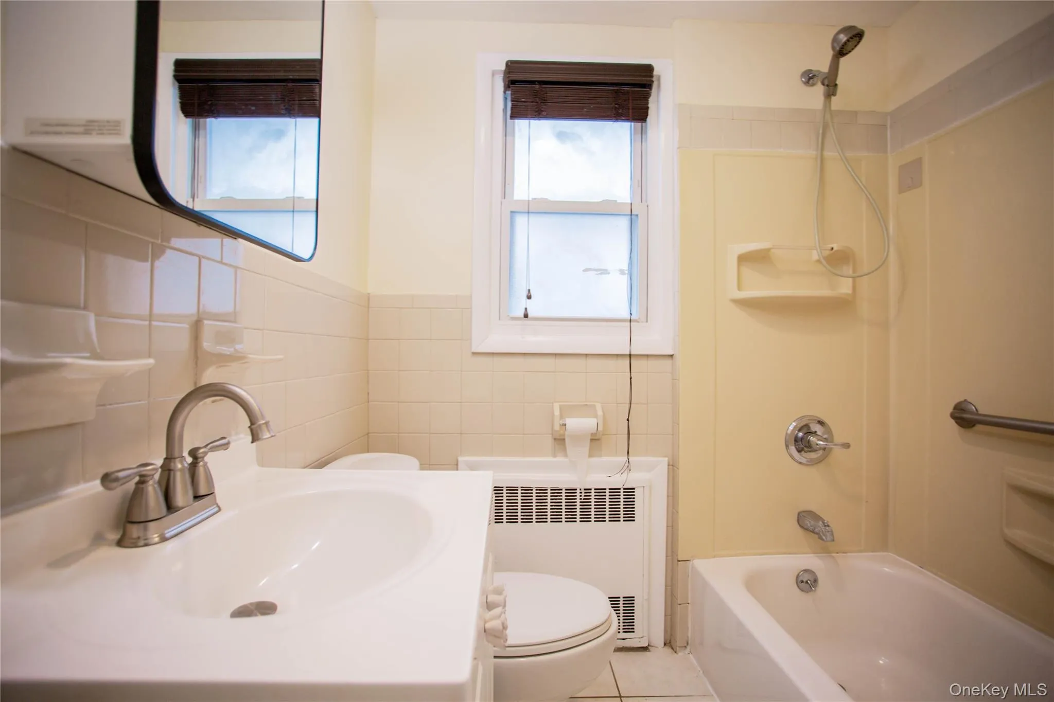 Bathroom with radiator heating unit, toilet, vanity, tile walls, and shower / tub combination Bathroom with radiator heating unit, toilet, vanity, tile walls, and shower / tub combination