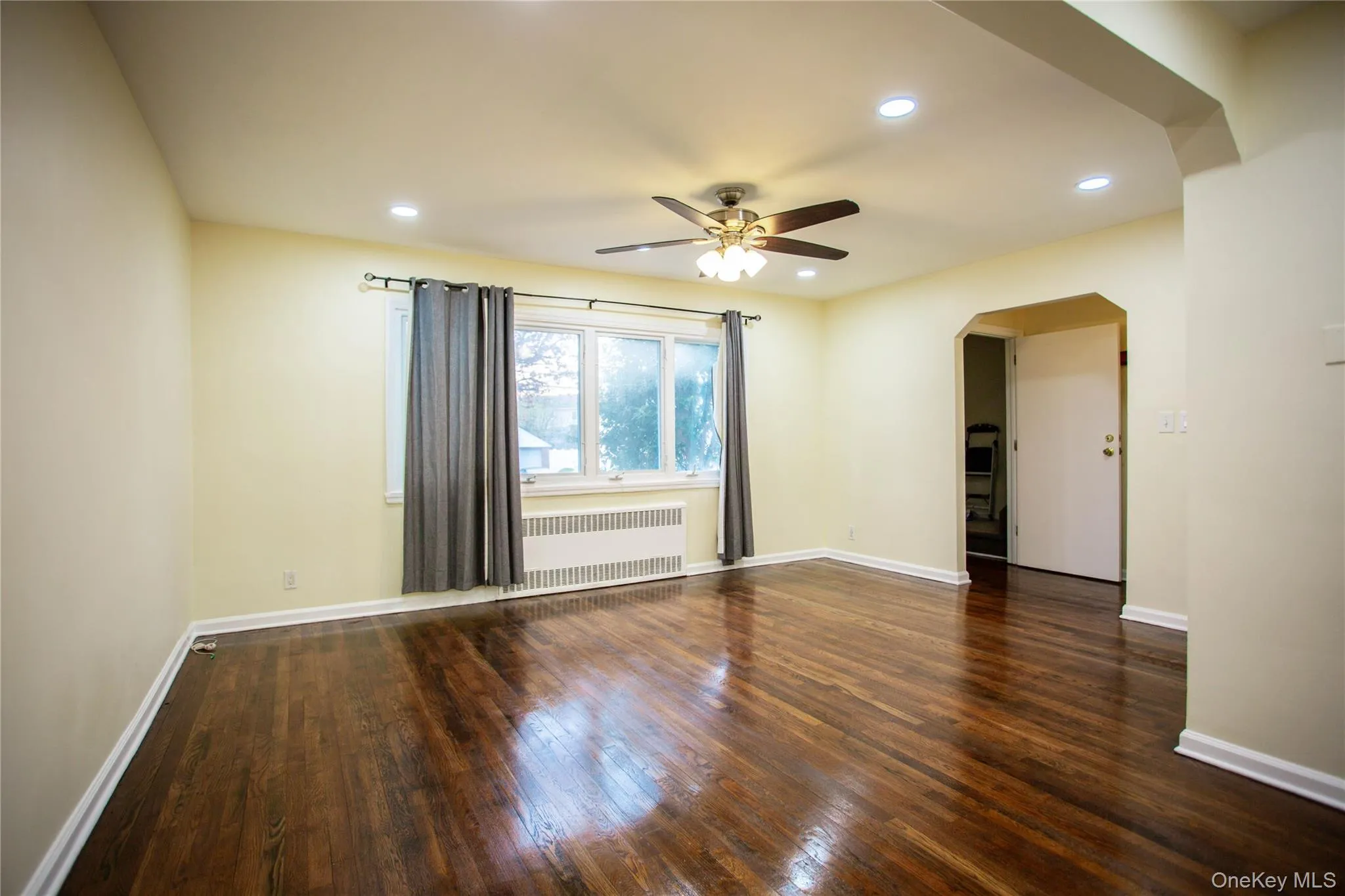 Empty room featuring radiator heating unit, a ceiling fan, arched walkways, and hardwood / wood-style flooring Empty room featuring radiator heating unit, a ceiling fan, arched walkways, and hardwood / wood-style flooring