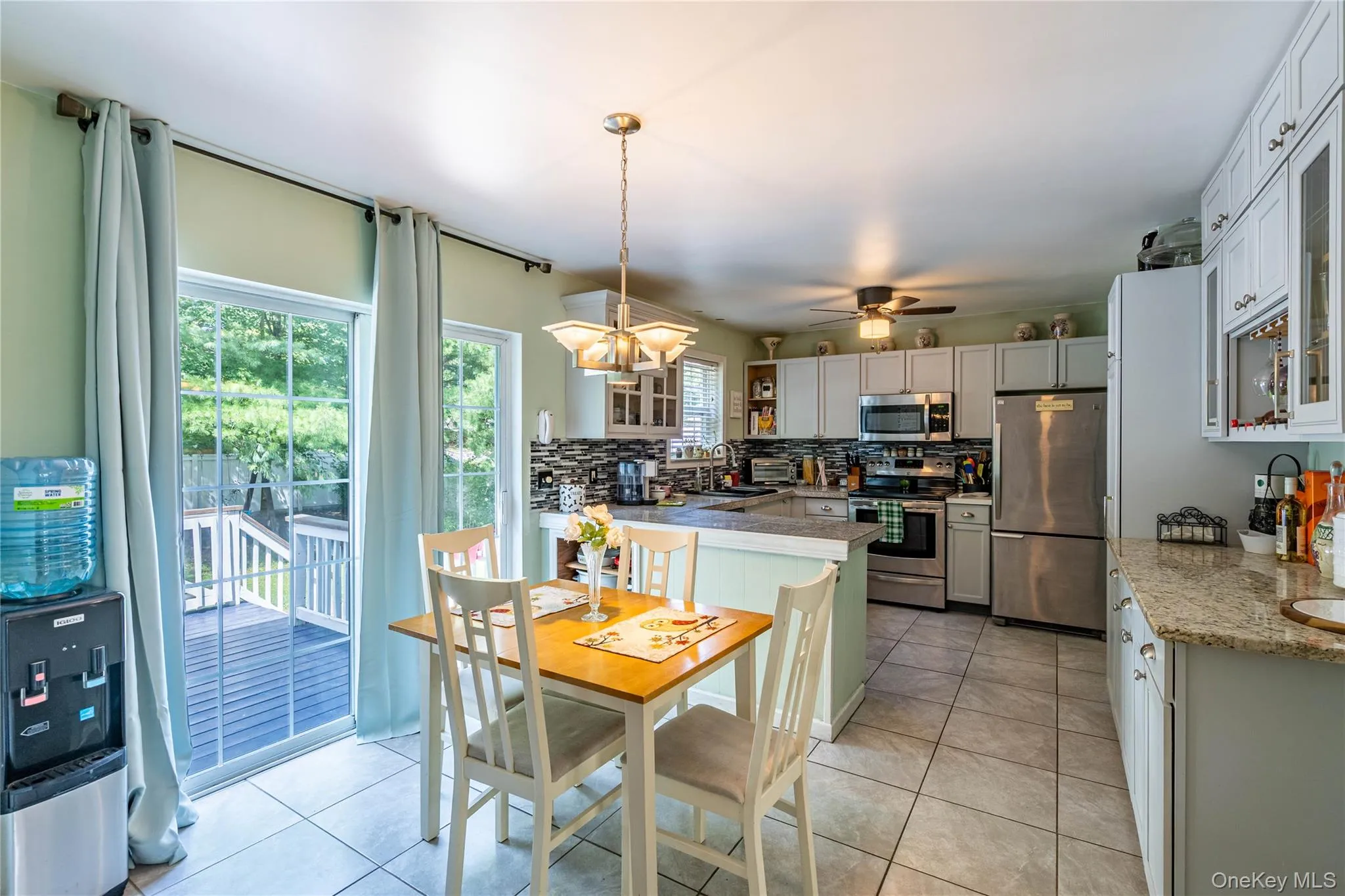Kitchen featuring glass insert cabinets, backsplash, stainless steel appliances, light tile patterned floors, and pendant lighting Kitchen featuring glass insert cabinets, backsplash, stainless steel appliances, light tile patterned floors, and pendant lighting