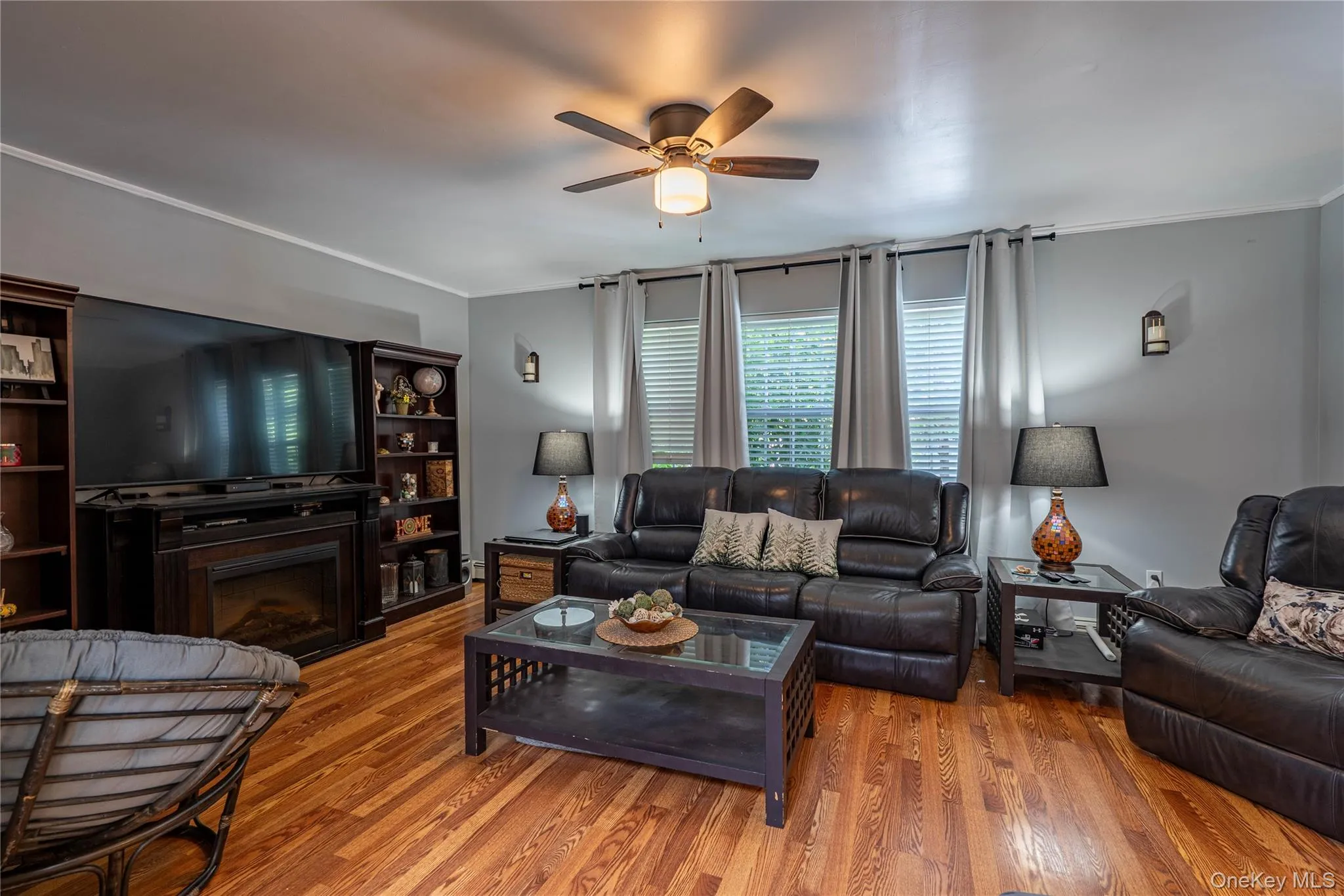 Living room with wood finished floors, a ceiling fan, a fireplace, and crown molding Living room with wood finished floors, a ceiling fan, a fireplace, and crown molding