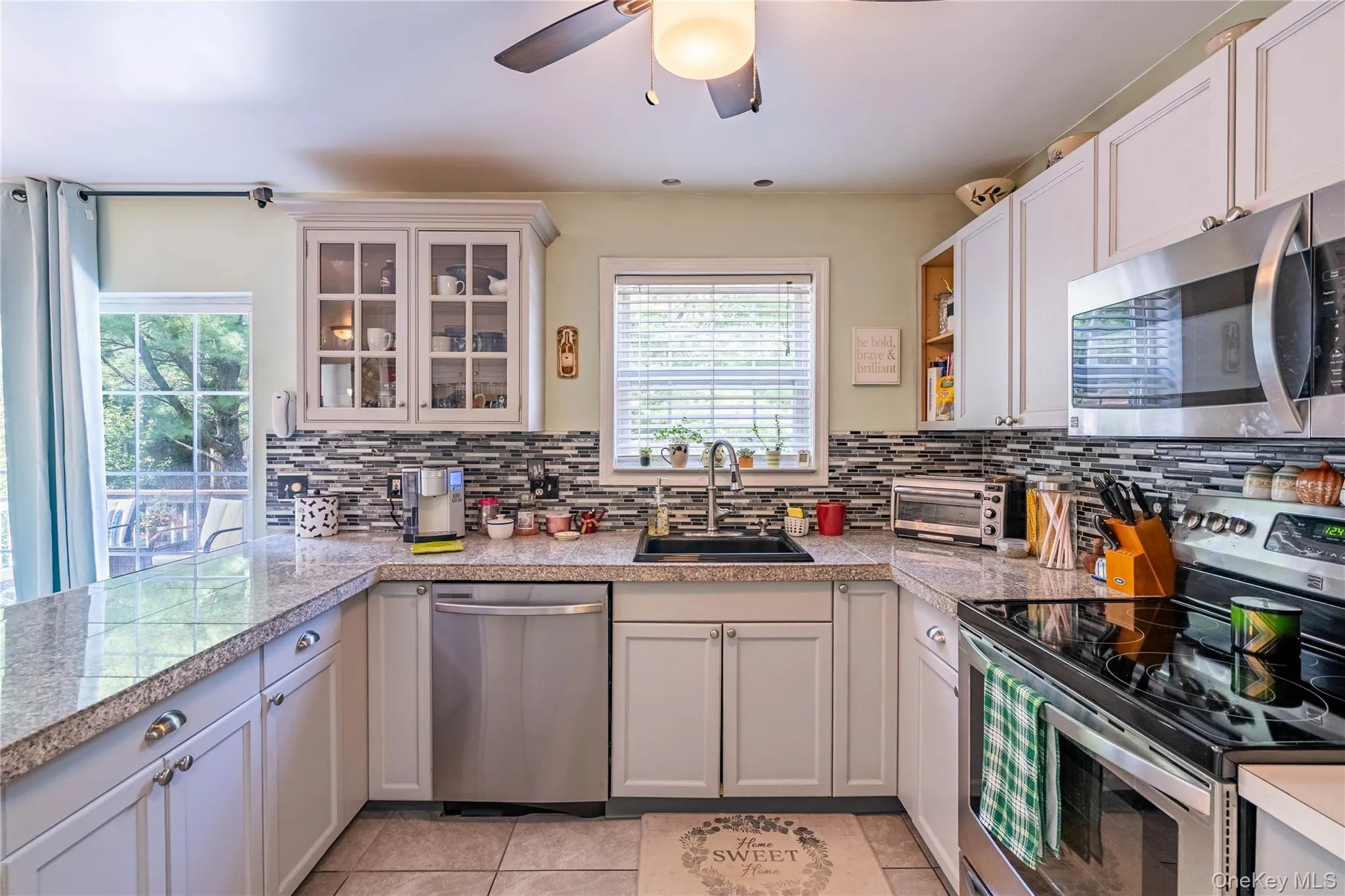 Kitchen featuring appliances with stainless steel finishes, tile counters, backsplash, light tile patterned floors, and glass insert cabinets Kitchen featuring appliances with stainless steel finishes, tile counters, backsplash, light tile patterned floors, and glass insert cabinets