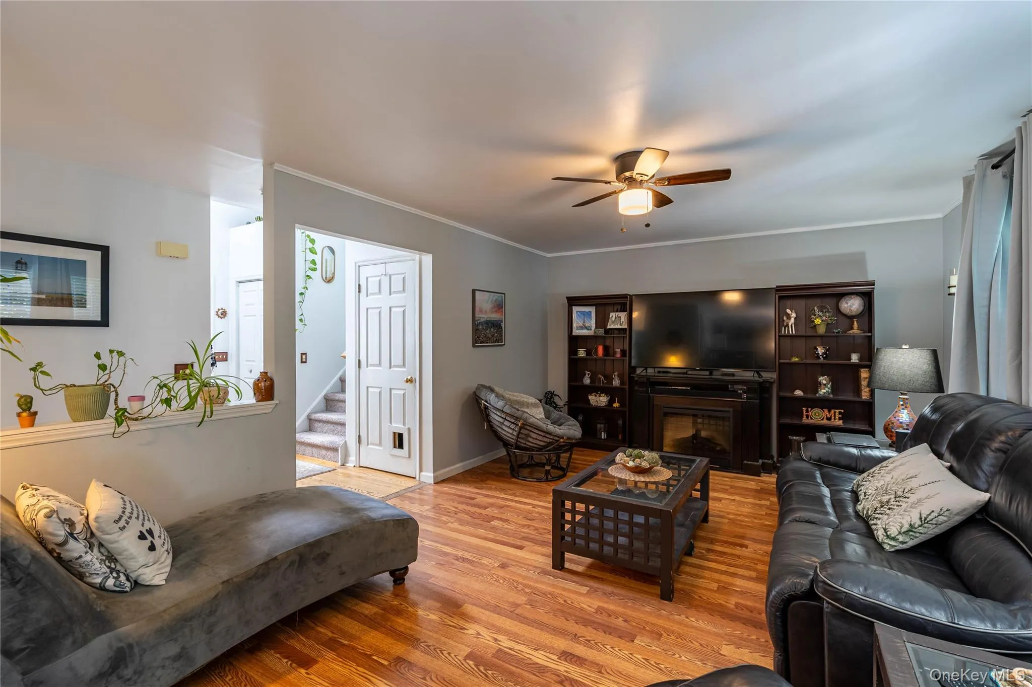 Living area featuring wood finished floors, ornamental molding, a fireplace, ceiling fan, and stairway Living area featuring wood finished floors, ornamental molding, a fireplace, ceiling fan, and stairway