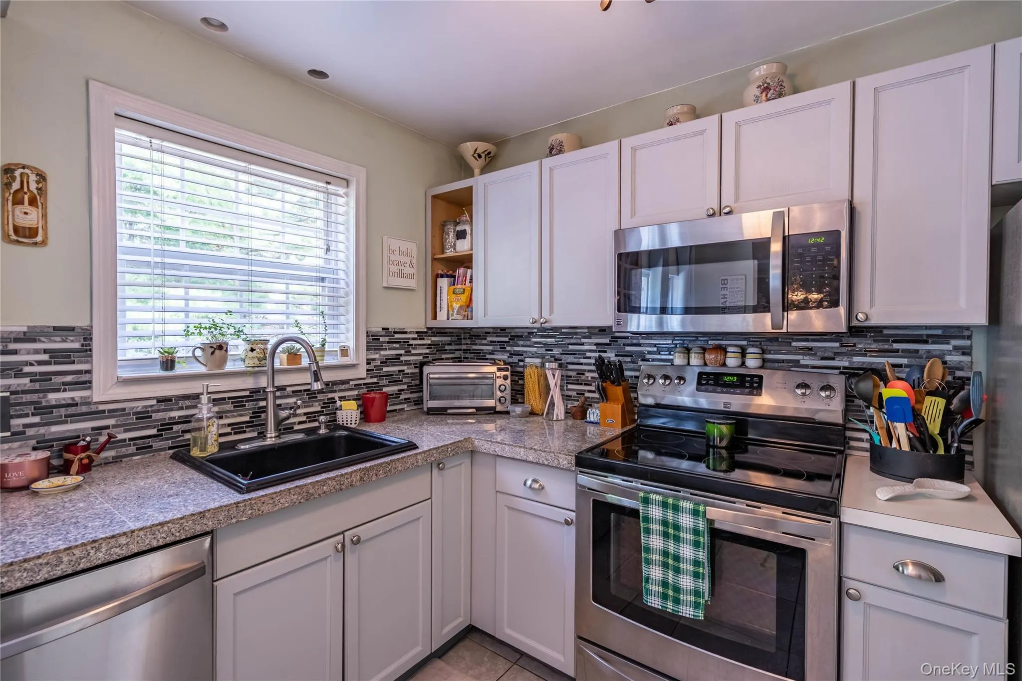 Kitchen featuring stainless steel appliances, tasteful backsplash, open shelves, tile counters, and light tile patterned floors Kitchen featuring stainless steel appliances, tasteful backsplash, open shelves, tile counters, and light tile patterned floors