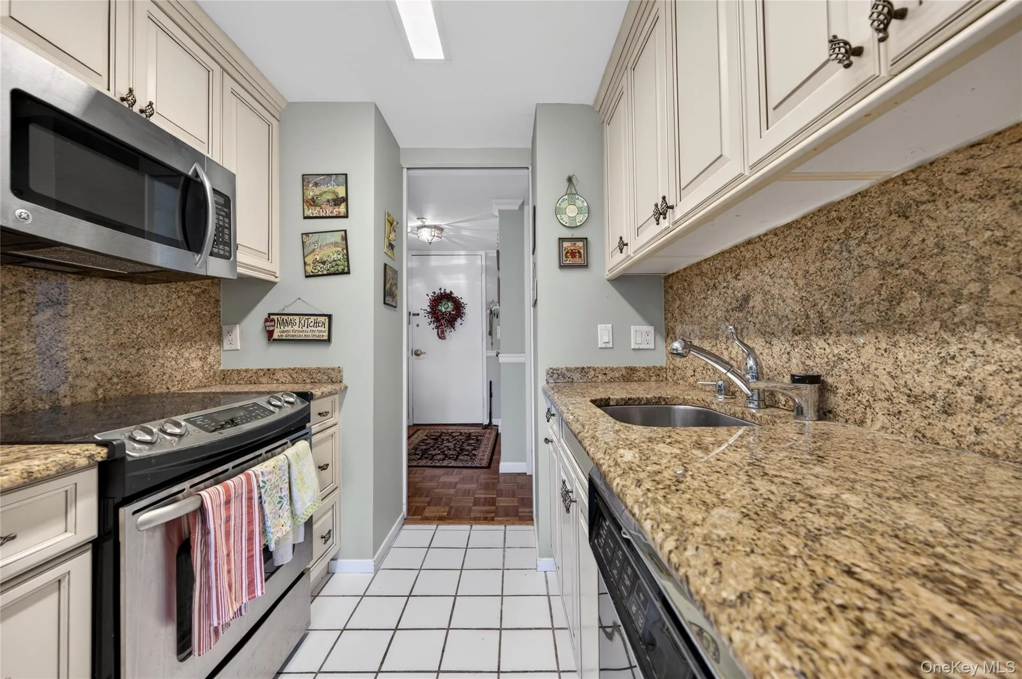 Galley kitchen featuring cream cabinetry, stainless steel appliances, granite countertops, and a matching granite backsplash Galley kitchen featuring cream cabinetry, stainless steel appliances, granite countertops, and a matching granite backsplash