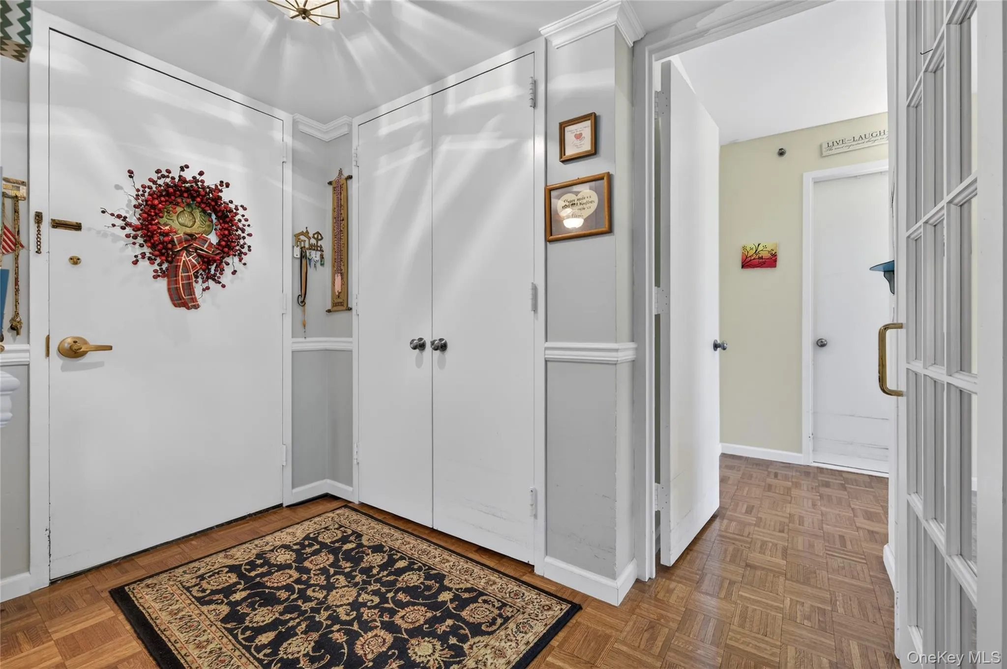 Entryway featuring parquet wood-finish flooring, white panel doors, and a built-in closet with double doors Entryway featuring parquet wood-finish flooring, white panel doors, and a built-in closet with double doors