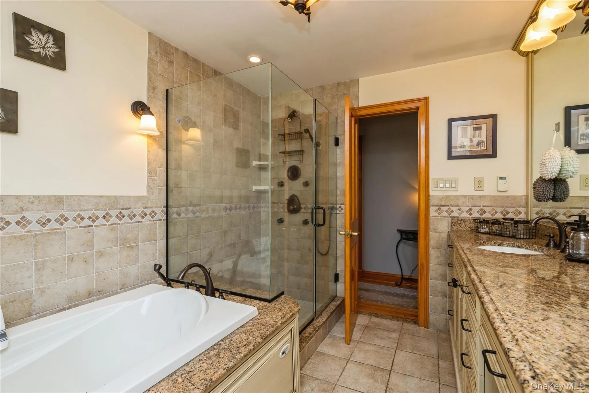 Bathroom featuring a frameless glass shower enclosure, a jetted soaking tub, a vanity with granite countertop, and tiled flooring Bathroom featuring a frameless glass shower enclosure, a jetted soaking tub, a vanity with granite countertop, and tiled flooring
