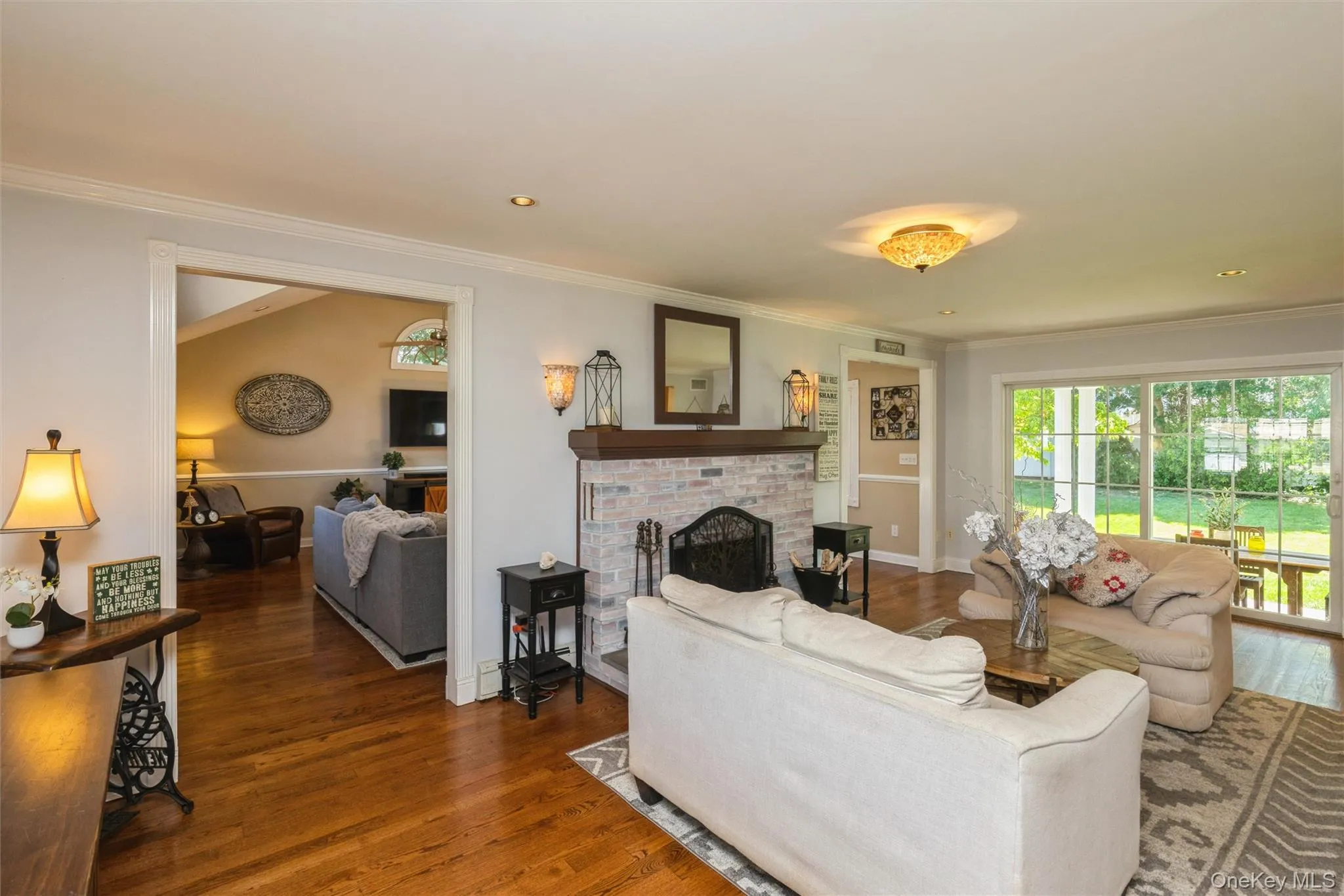 Living area featuring hardwood flooring, a brick-surround fireplace with wood mantel, recessed lighting, and crown molding Living area featuring hardwood flooring, a brick-surround fireplace with wood mantel, recessed lighting, and crown molding