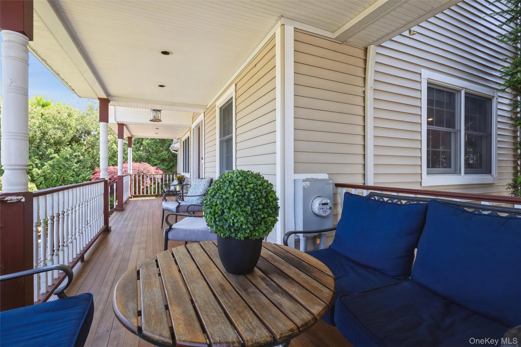 Expansive covered porch featuring Mahogany finish flooring, white spindle railings with a dark base, recessed lighting, and a light-colored siding exterior Expansive covered porch featuring Mahogany finish flooring, white spindle railings with a dark base, recessed lighting, and a light-colored siding exterior