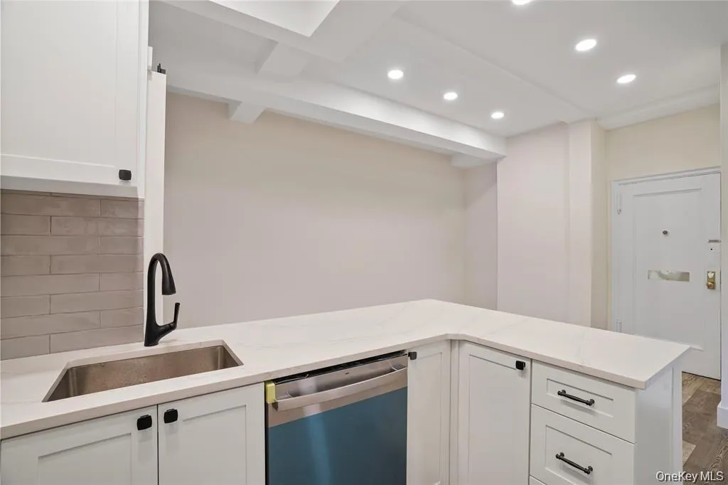 Modern kitchen featuring white shaker cabinetry with black hardware, an undermount stainless steel sink with a matte black faucet, and light-toned countertops Modern kitchen featuring white shaker cabinetry with black hardware, an undermount stainless steel sink with a matte black faucet, and light-toned countertops