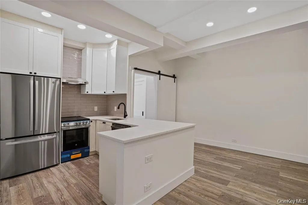 Open-concept living space featuring wood-finish flooring, a contemporary kitchen island with a white countertop, and recessed lighting Open-concept living space featuring wood-finish flooring, a contemporary kitchen island with a white countertop, and recessed lighting