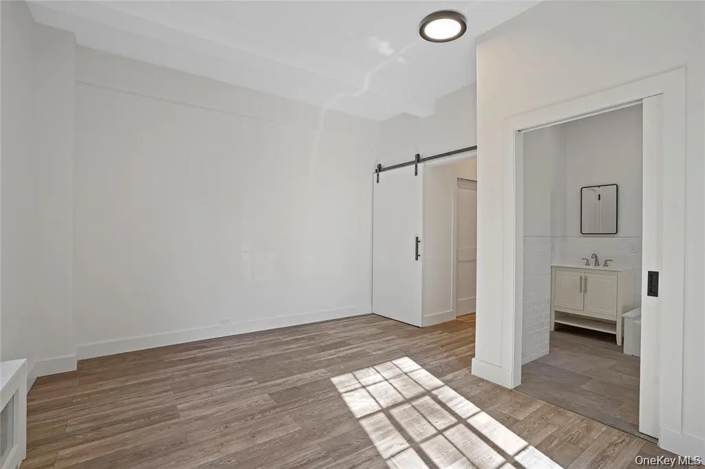 Spacious room featuring wood-finish flooring, recessed lighting, and a barn door entry Spacious room featuring wood-finish flooring, recessed lighting, and a barn door entry
