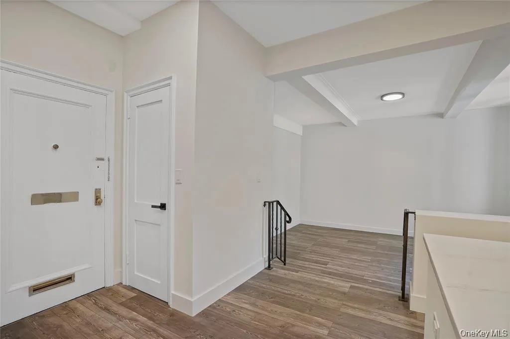 Entryway with wood-finish flooring, two white panel doors, and a partial staircase featuring a black metal railing Entryway with wood-finish flooring, two white panel doors, and a partial staircase featuring a black metal railing