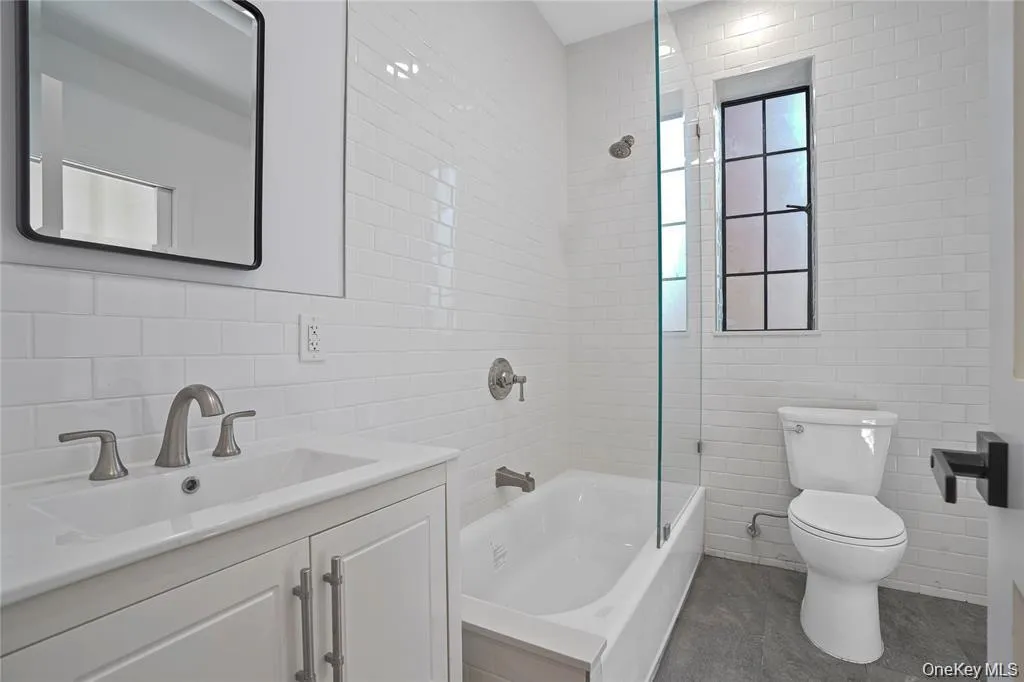 Bathroom featuring white subway tile walls, a vanity with an integrated sink, brushed nickel fixtures, a glass shower partition, and a black-framed window Bathroom featuring white subway tile walls, a vanity with an integrated sink, brushed nickel fixtures, a glass shower partition, and a black-framed window