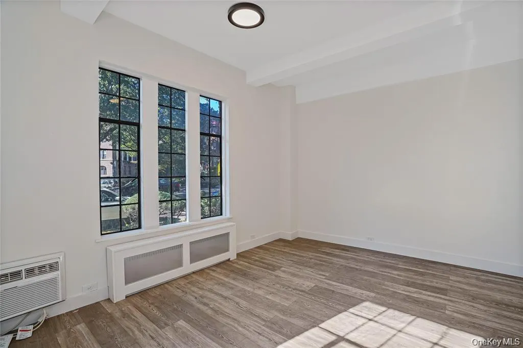 Triple pane windows with dark sashes, wood-finish flooring, ceiling-mounted light fixture, and white painted walls Triple pane windows with dark sashes, wood-finish flooring, ceiling-mounted light fixture, and white painted walls