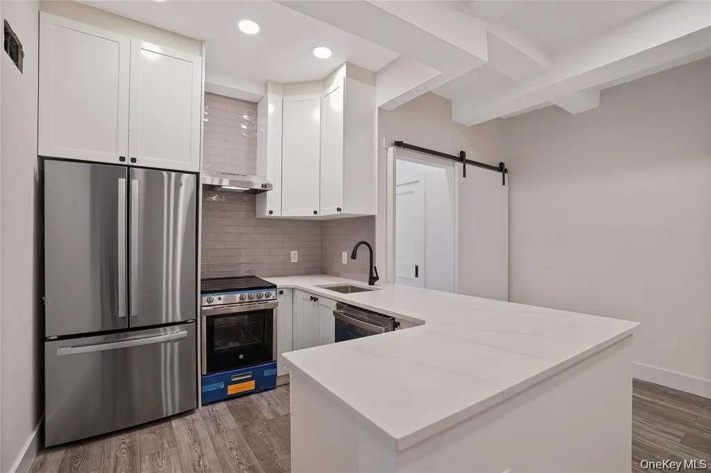 Kitchen featuring white shaker cabinetry, stainless steel appliances, light-colored countertops, and wood-finish flooring Kitchen featuring white shaker cabinetry, stainless steel appliances, light-colored countertops, and wood-finish flooring