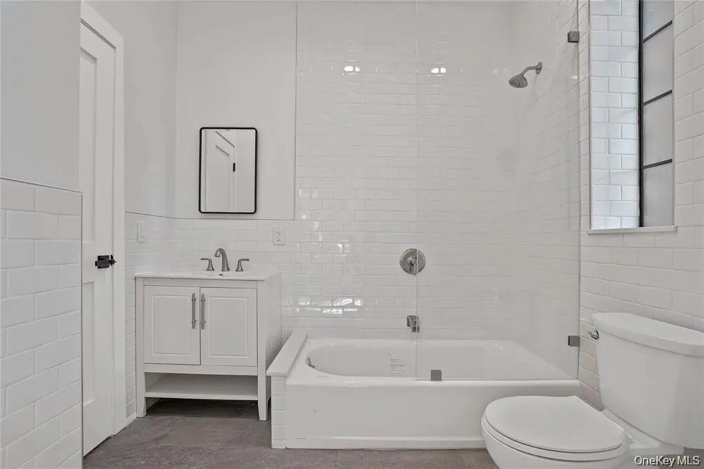 Modern bathroom featuring white subway tile, a freestanding vanity with a basin sink, a bathtub with an overhead shower, a glass shower partition, and a black-framed wall mirror Modern bathroom featuring white subway tile, a freestanding vanity with a basin sink, a bathtub with an overhead shower, a glass shower partition, and a black-framed wall mirror