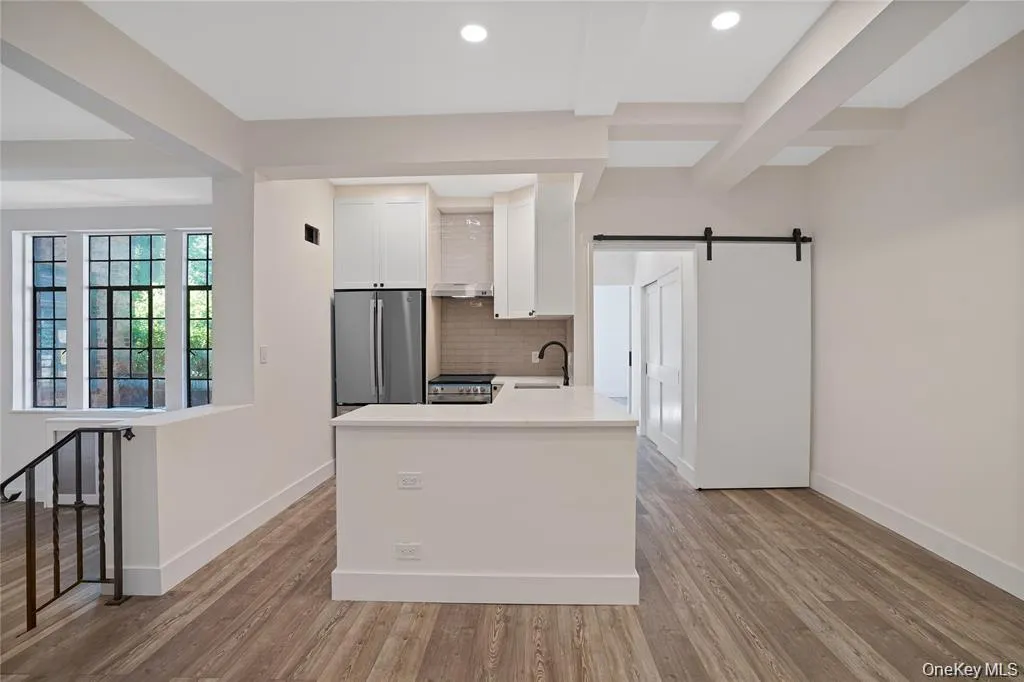 Open-concept living space featuring wood-finish flooring, a contemporary kitchen island with a white countertop, and recessed lighting Open-concept living space featuring wood-finish flooring, a contemporary kitchen island with a white countertop, and recessed lighting