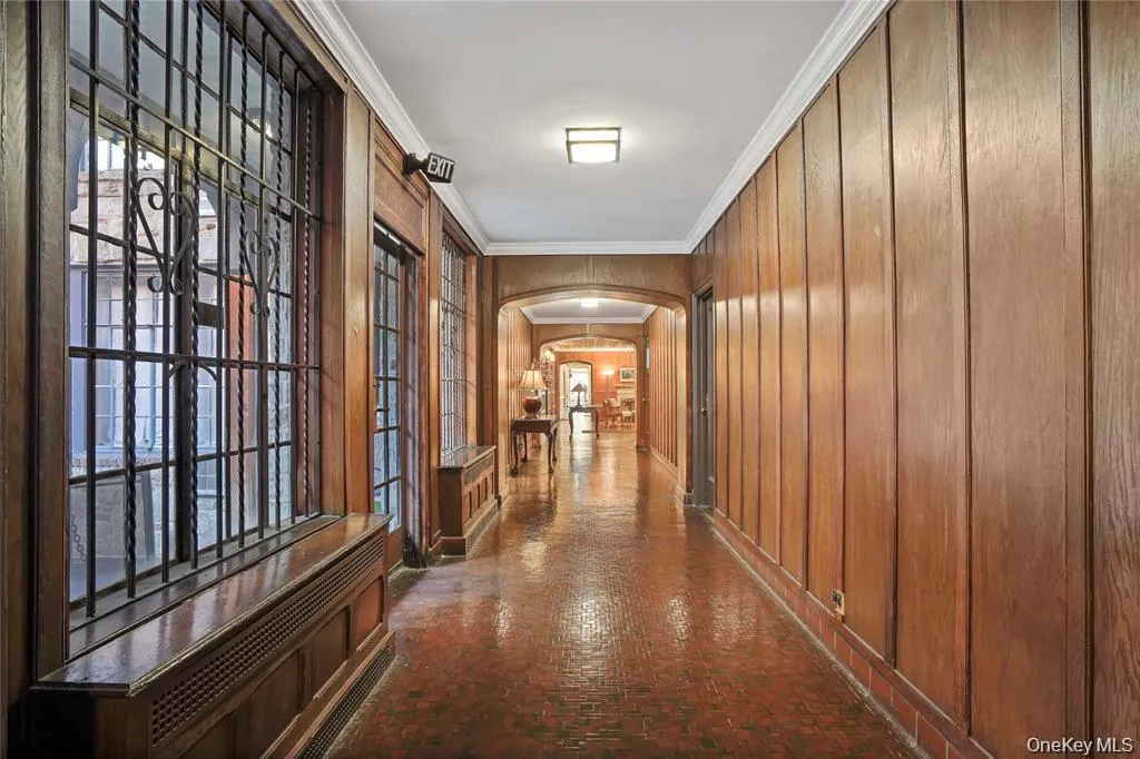 Long hallway featuring wood-paneled walls and a tiled floor Long hallway featuring wood-paneled walls and a tiled floor