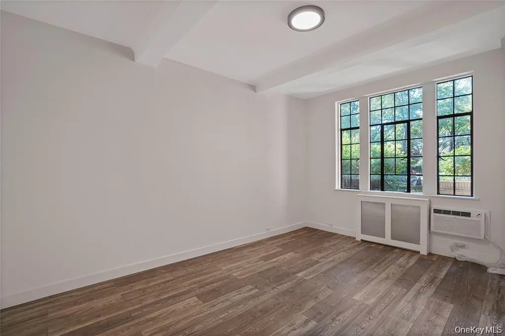 Bright room featuring three large windows, wood-finish flooring, and a flush-mount ceiling light Bright room featuring three large windows, wood-finish flooring, and a flush-mount ceiling light