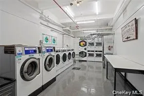 On-site laundry facility featuring multiple front-loading washers and dryers, a dedicated folding counter, and bright overhead lighting On-site laundry facility featuring multiple front-loading washers and dryers, a dedicated folding counter, and bright overhead lighting