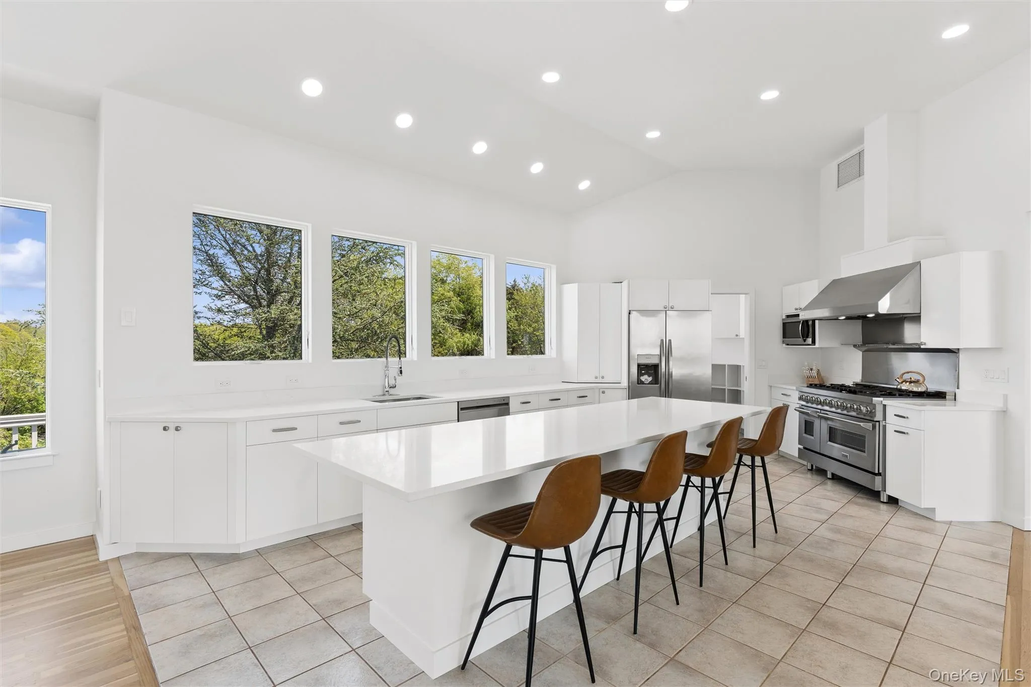 Spacious kitchen featuring an extended island, white cabinetry, integrated stainless steel appliances, a professional-grade range with a stainless steel vent hood, and abundant natural light from multiple windows Spacious kitchen featuring an extended island, white cabinetry, integrated stainless steel appliances, a professional-grade range with a stainless steel vent hood, and abundant natural light from multiple windows