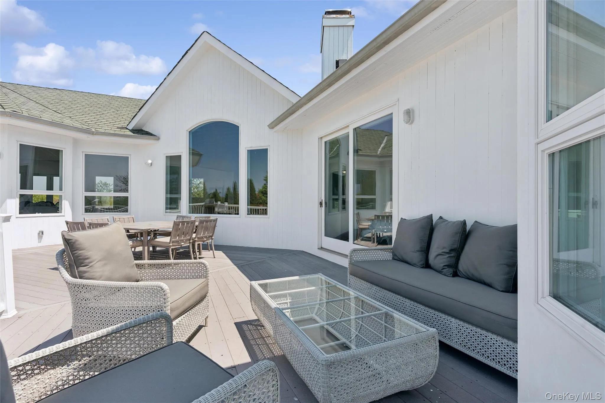 Expansive wrap around exterior deck featuring composite decking, white siding, multiple large windows, and a sliding glass door Expansive wrap around exterior deck featuring composite decking, white siding, multiple large windows, and a sliding glass door