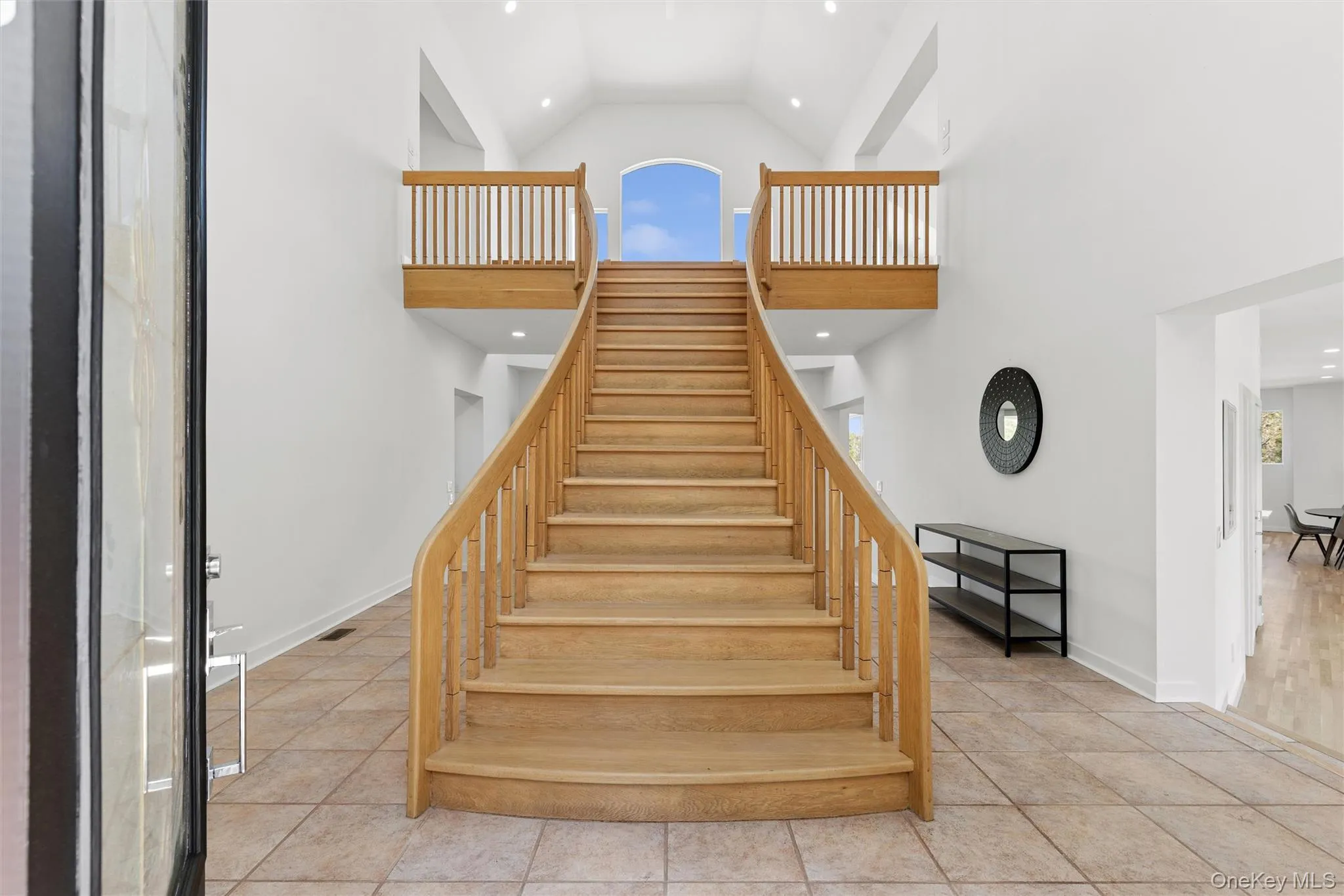 Two-story foyer featuring a grand wooden staircase with dual landings, vaulted ceilings, recessed lighting, and tile flooring Two-story foyer featuring a grand wooden staircase with dual landings, vaulted ceilings, recessed lighting, and tile flooring