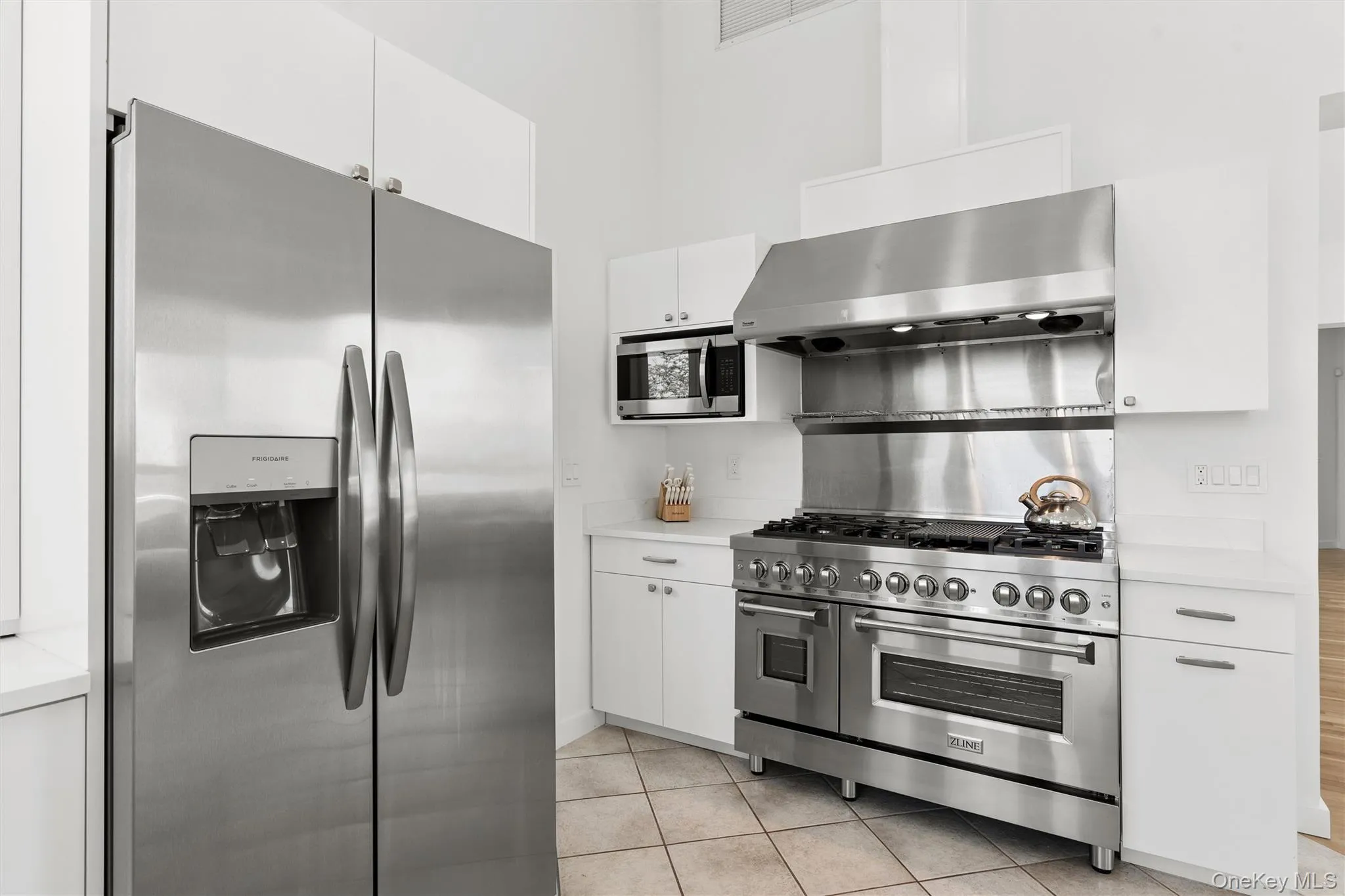 2nd Floor Kitchen featuring stainless steel appliances, white cabinetry, a six-burner range with griddle, matching range hood, and tile flooring 2nd Floor Kitchen featuring stainless steel appliances, white cabinetry, a six-burner range with griddle, matching range hood, and tile flooring