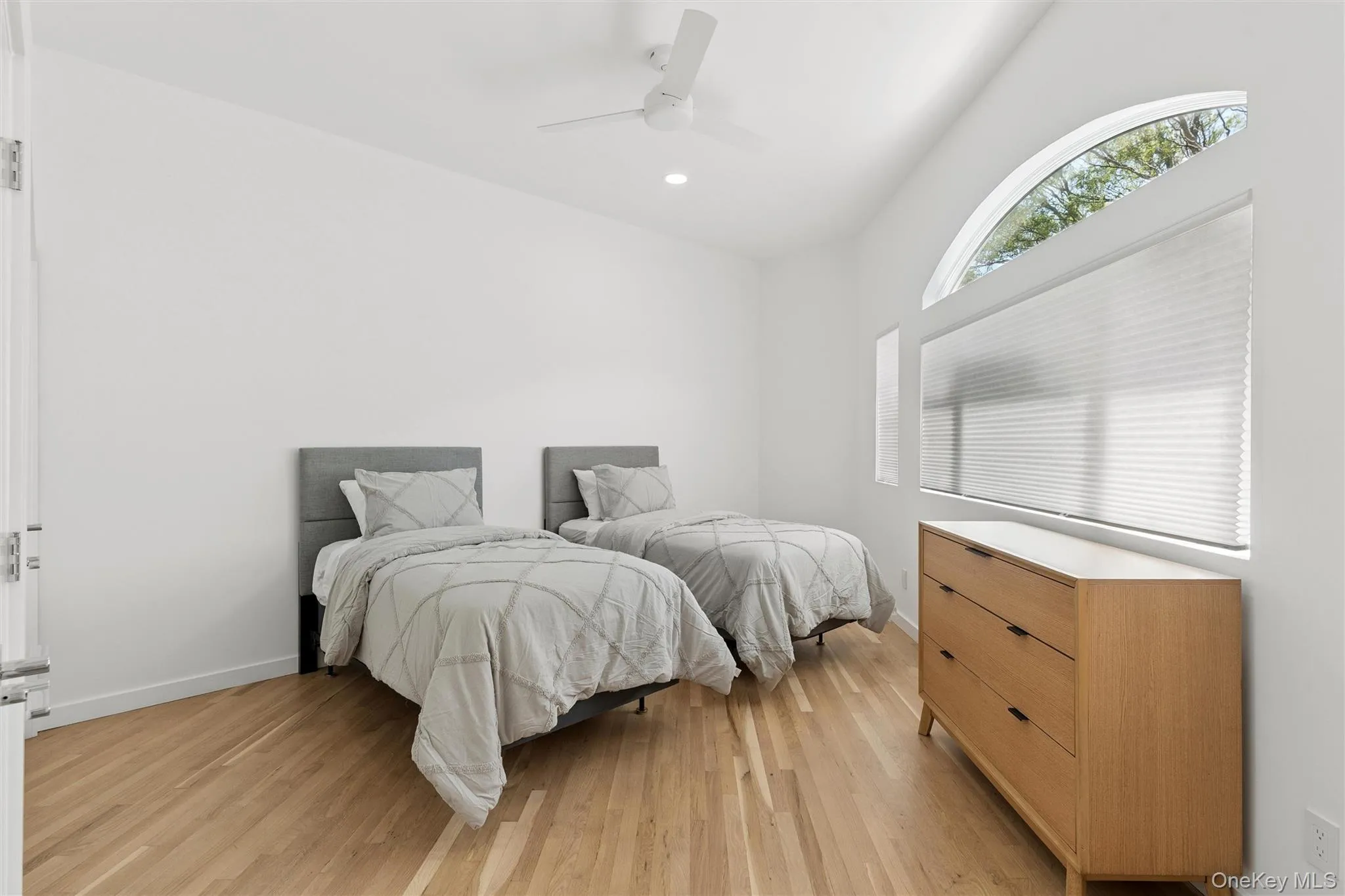 Vaulted ceiling room featuring natural wood-finish flooring, a large arched window, and a ceiling fan Vaulted ceiling room featuring natural wood-finish flooring, a large arched window, and a ceiling fan
