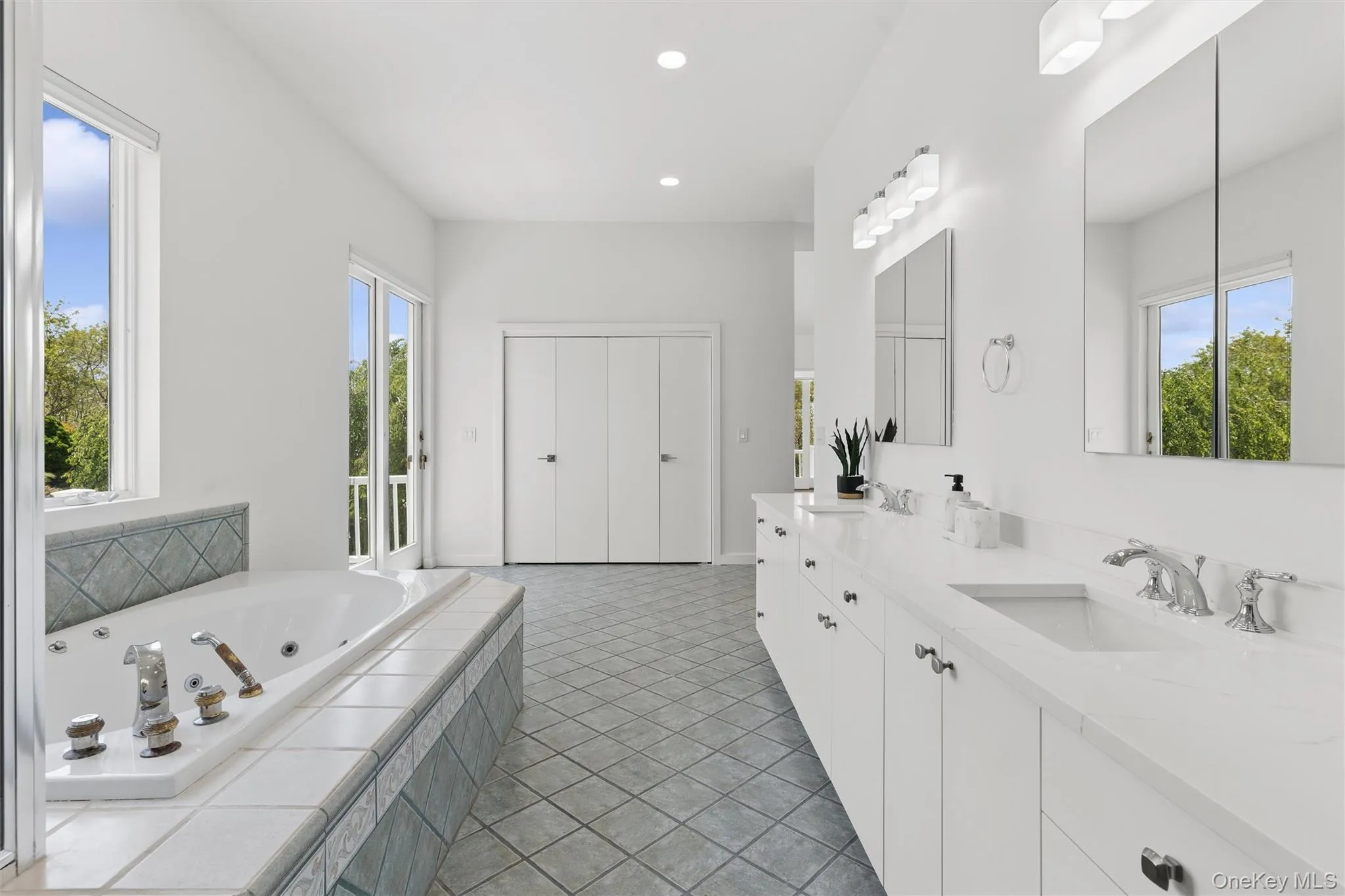 Spacious bath featuring dual vanities with integrated sinks, a built-in jetted tub with tiled surround, and a walk-out balcony Spacious bath featuring dual vanities with integrated sinks, a built-in jetted tub with tiled surround, and a walk-out balcony