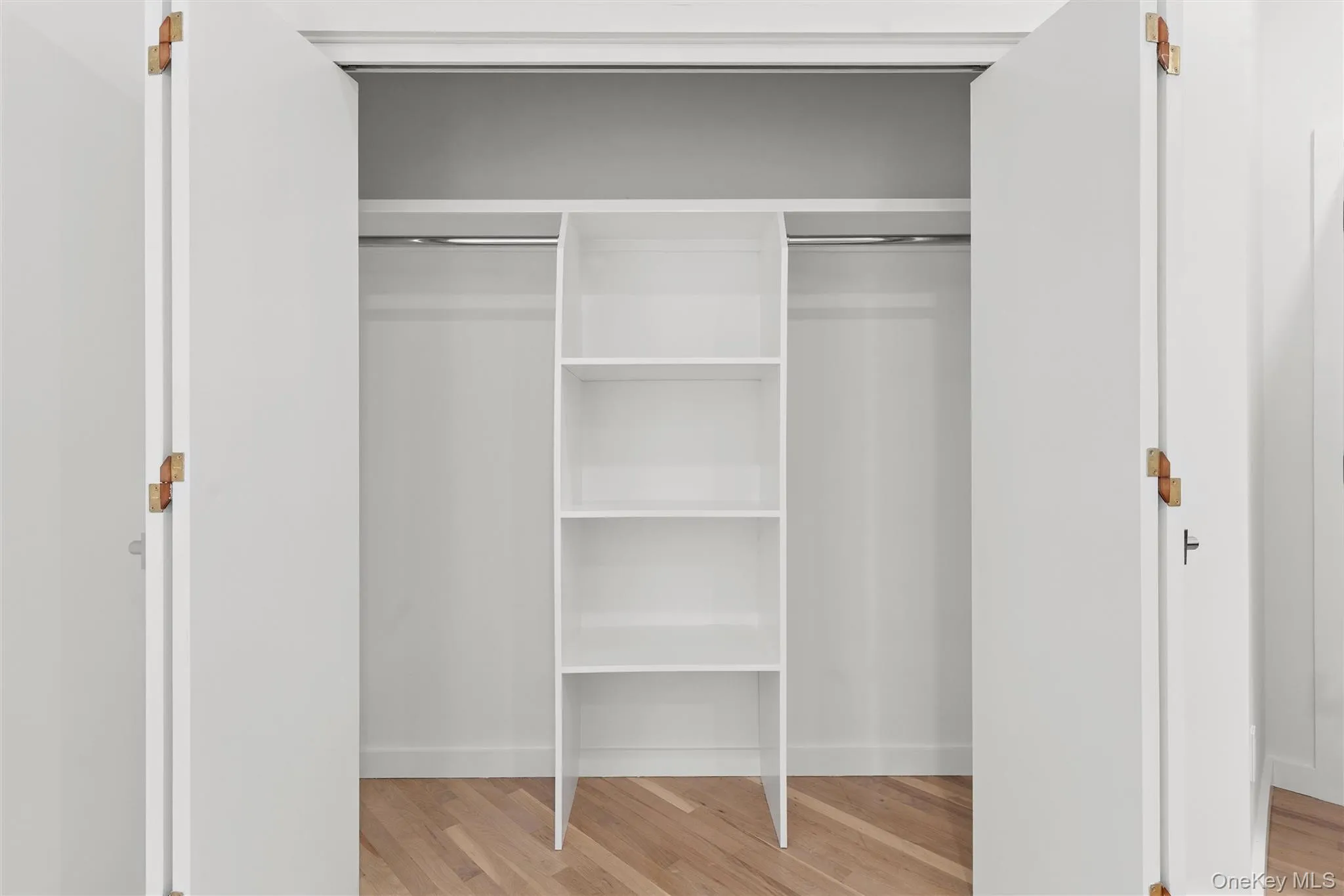 Bifold closet doors revealing built-in shelving, two hanging rods, and wood-finish flooring Bifold closet doors revealing built-in shelving, two hanging rods, and wood-finish flooring
