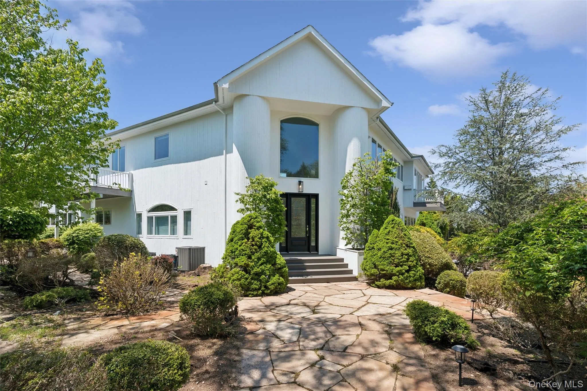 Front exterior featuring a prominent gabled entrance with a tall arched window, framed by large fluted columns Front exterior featuring a prominent gabled entrance with a tall arched window, framed by large fluted columns