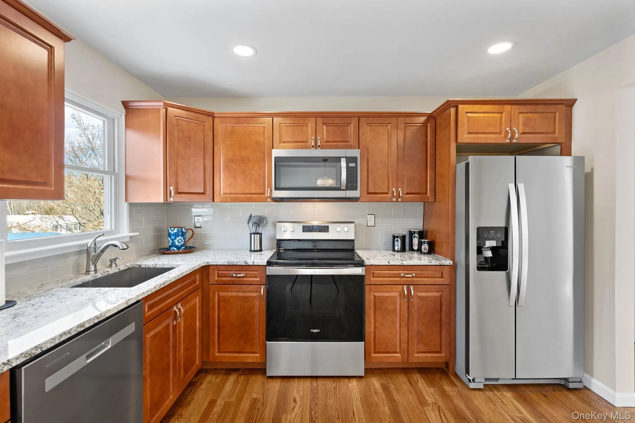 Kitchen with sink, light hardwood / wood-style flooring, stainless steel appliances, tasteful backsplash, and light stone counters Kitchen with sink, light hardwood / wood-style flooring, stainless steel appliances, tasteful backsplash, and light stone counters