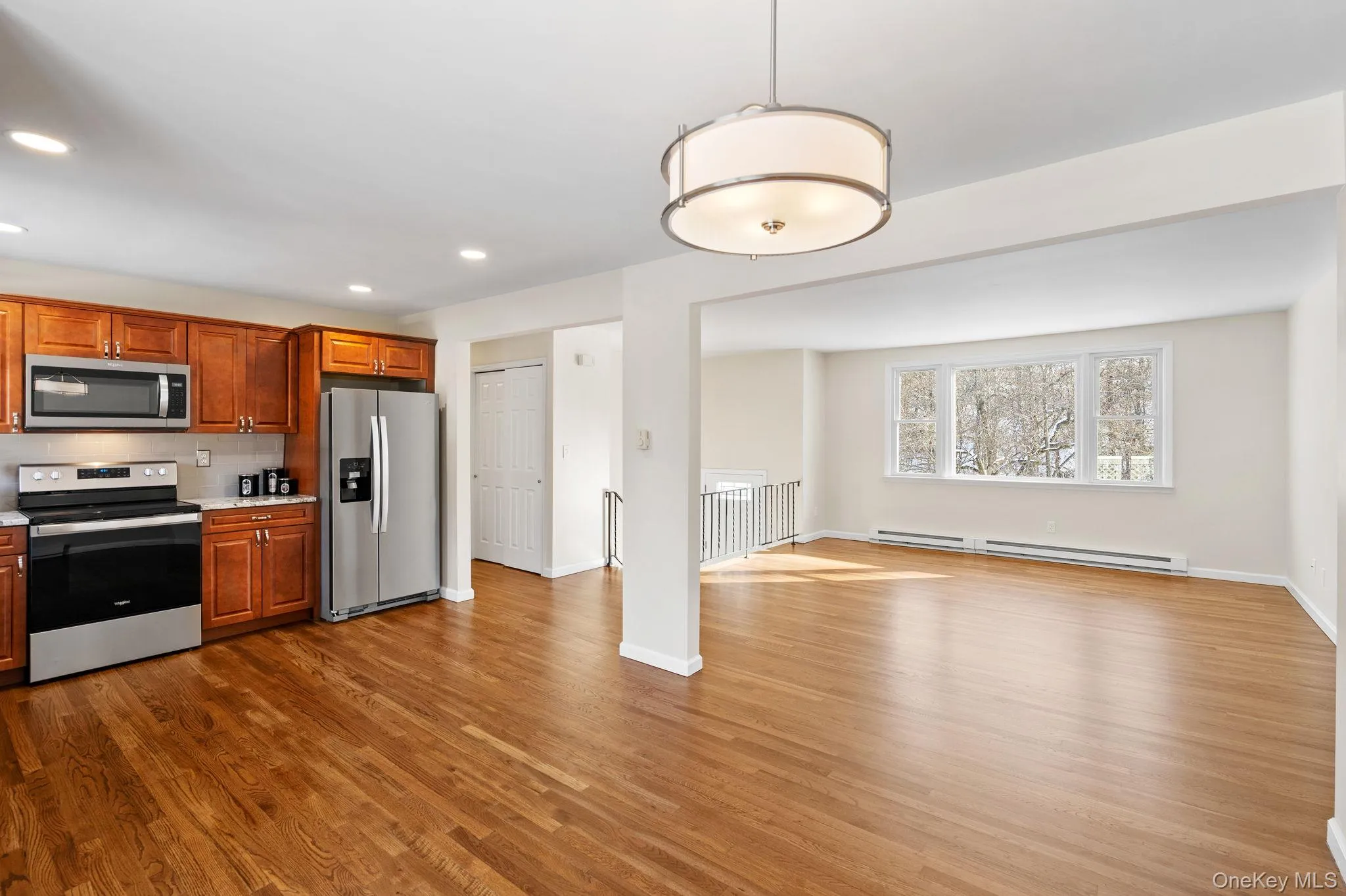 Kitchen with baseboard heating, appliances with stainless steel finishes, hanging light fixtures, and wood-type flooring Kitchen with baseboard heating, appliances with stainless steel finishes, hanging light fixtures, and wood-type flooring