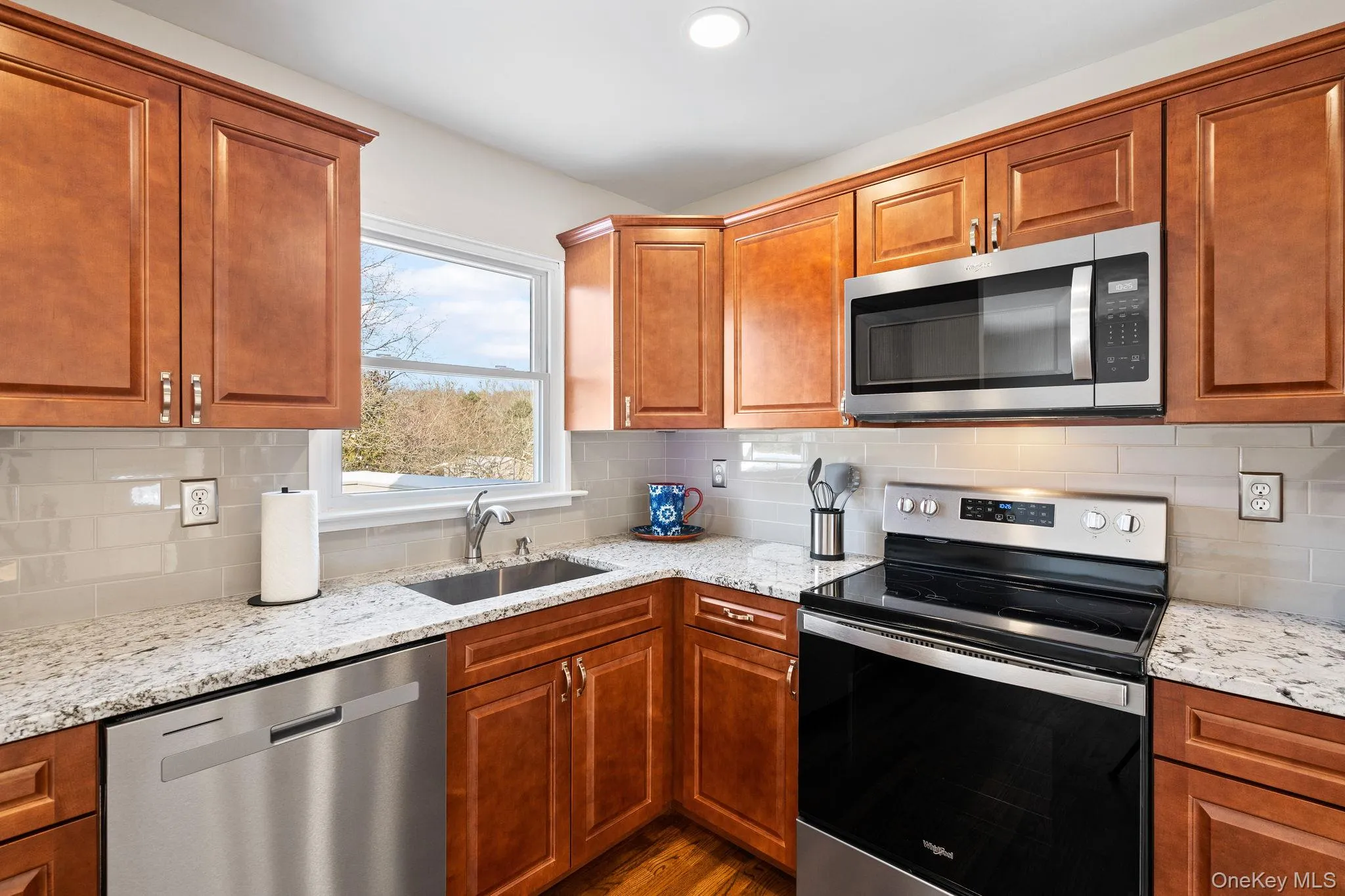 Kitchen with sink, backsplash, light stone countertops, and appliances with stainless steel finishes Kitchen with sink, backsplash, light stone countertops, and appliances with stainless steel finishes
