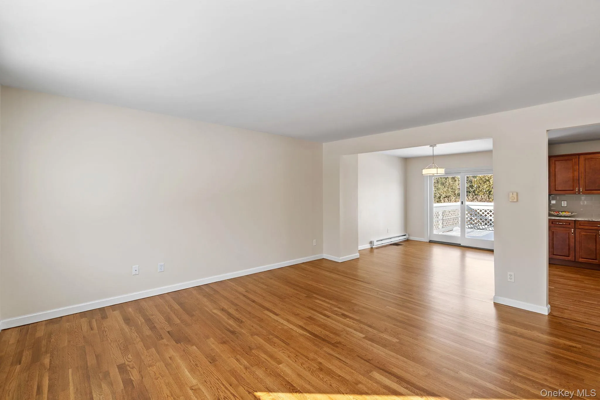 Unfurnished living room with a baseboard radiator and light hardwood / wood-style floors Unfurnished living room with a baseboard radiator and light hardwood / wood-style floors