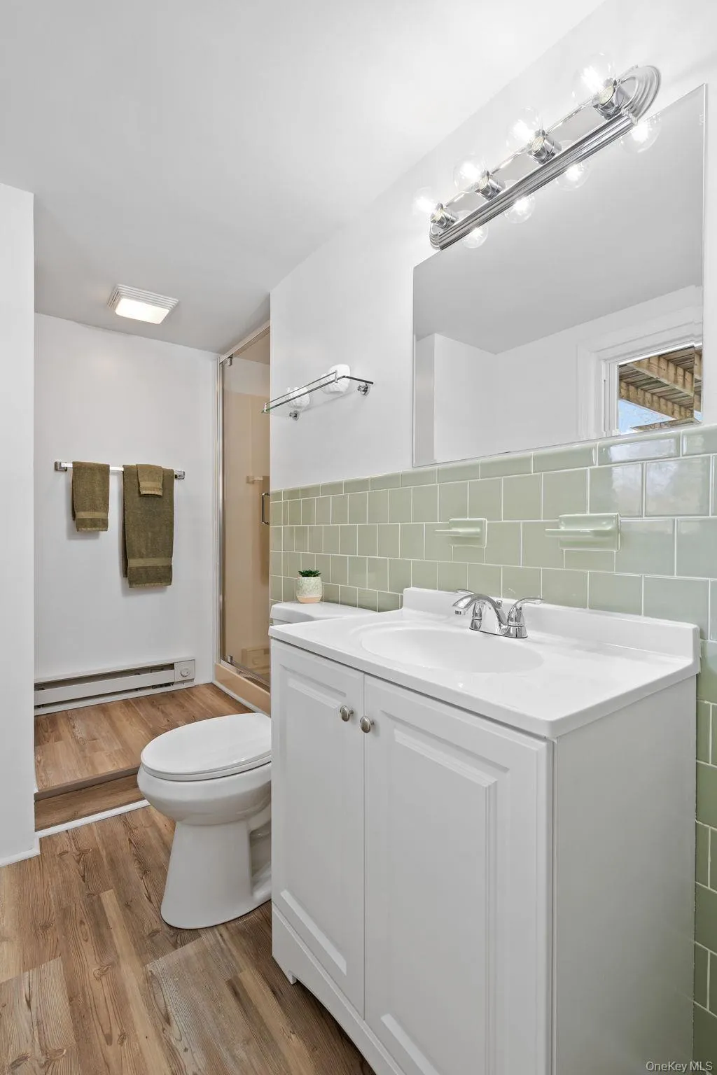 Bathroom featuring walk in shower, tile walls, a baseboard radiator, vanity, and hardwood / wood-style flooring Bathroom featuring walk in shower, tile walls, a baseboard radiator, vanity, and hardwood / wood-style flooring