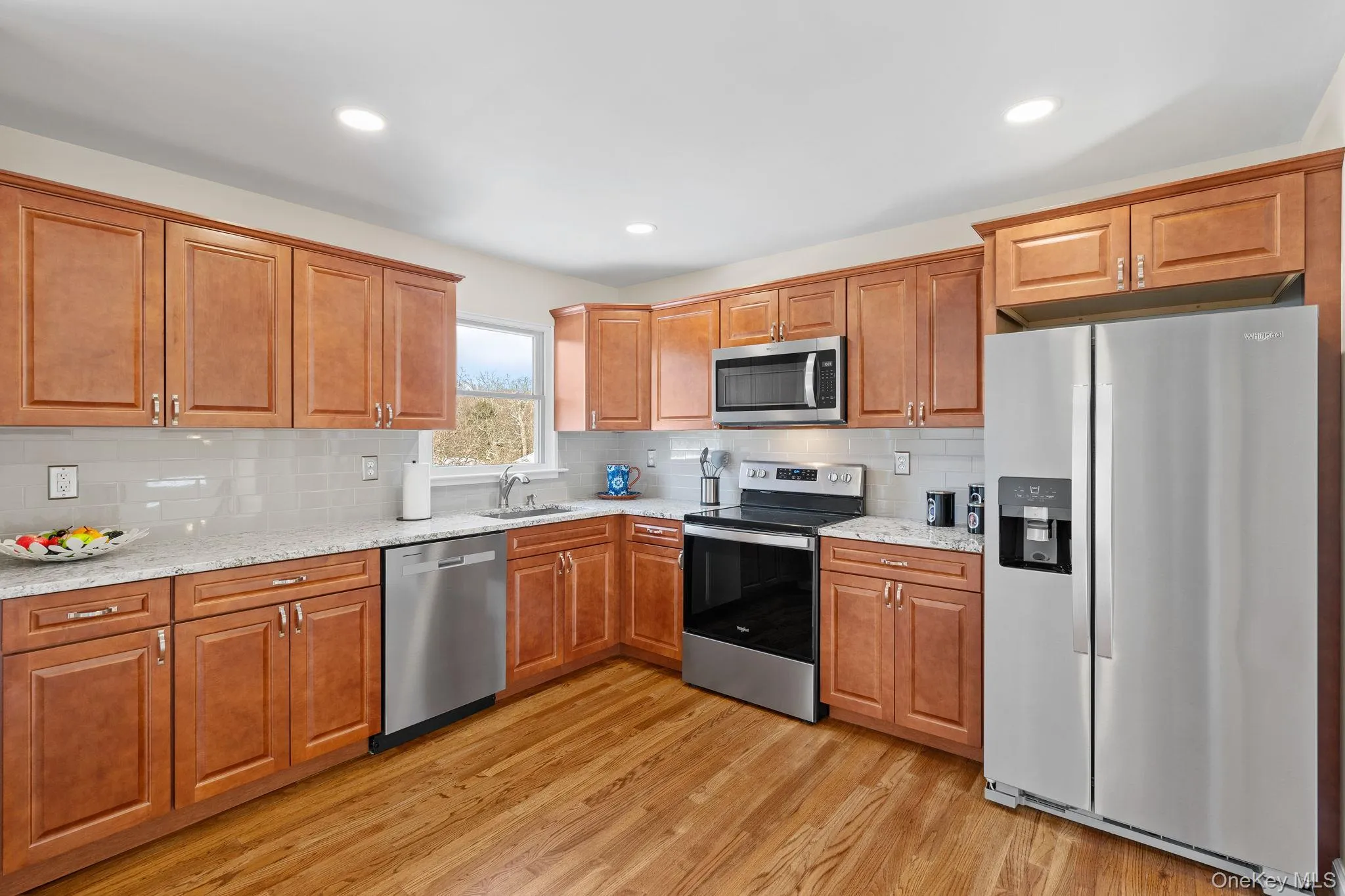 Kitchen featuring light stone countertops, decorative backsplash, light hardwood / wood-style floors, and appliances with stainless steel finishes Kitchen featuring light stone countertops, decorative backsplash, light hardwood / wood-style floors, and appliances with stainless steel finishes