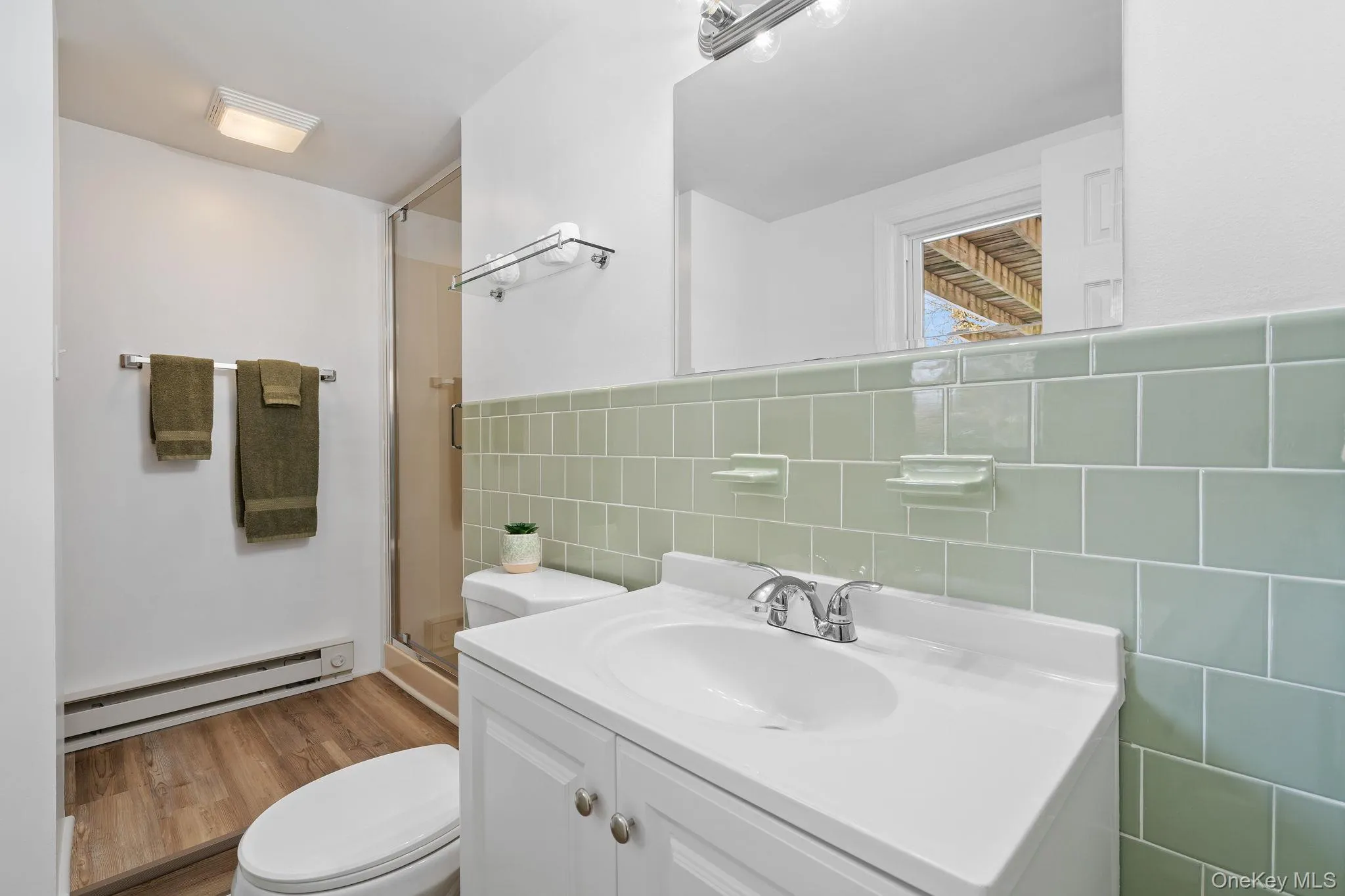 Bathroom featuring tile walls, an enclosed shower, vanity, a baseboard radiator, and toilet Bathroom featuring tile walls, an enclosed shower, vanity, a baseboard radiator, and toilet