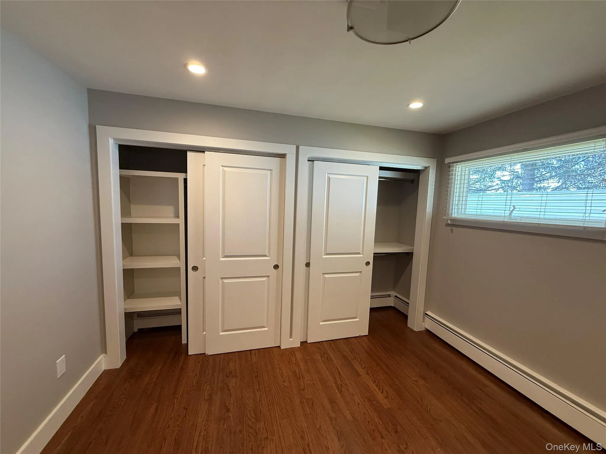 Unfurnished bedroom featuring recessed lighting, a baseboard heating unit, dark wood-style flooring, and two closets Unfurnished bedroom featuring recessed lighting, a baseboard heating unit, dark wood-style flooring, and two closets
