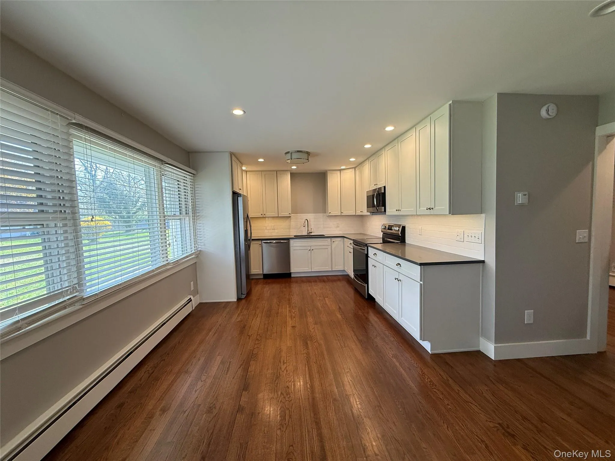 Kitchen featuring tasteful backsplash, baseboard heating, dark wood finished floors, a sink, and stainless steel appliances Kitchen featuring tasteful backsplash, baseboard heating, dark wood finished floors, a sink, and stainless steel appliances