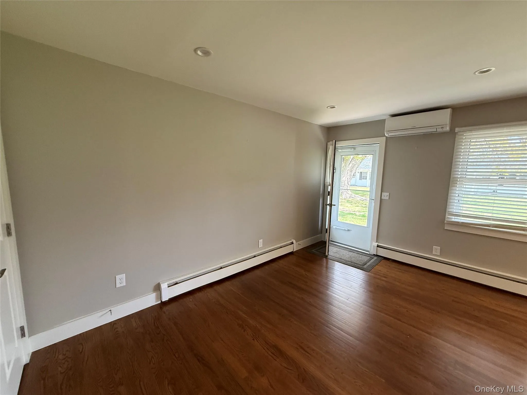 Unfurnished room with wood finished floors, recessed lighting, a wall mounted AC, and a baseboard heating unit Unfurnished room with wood finished floors, recessed lighting, a wall mounted AC, and a baseboard heating unit