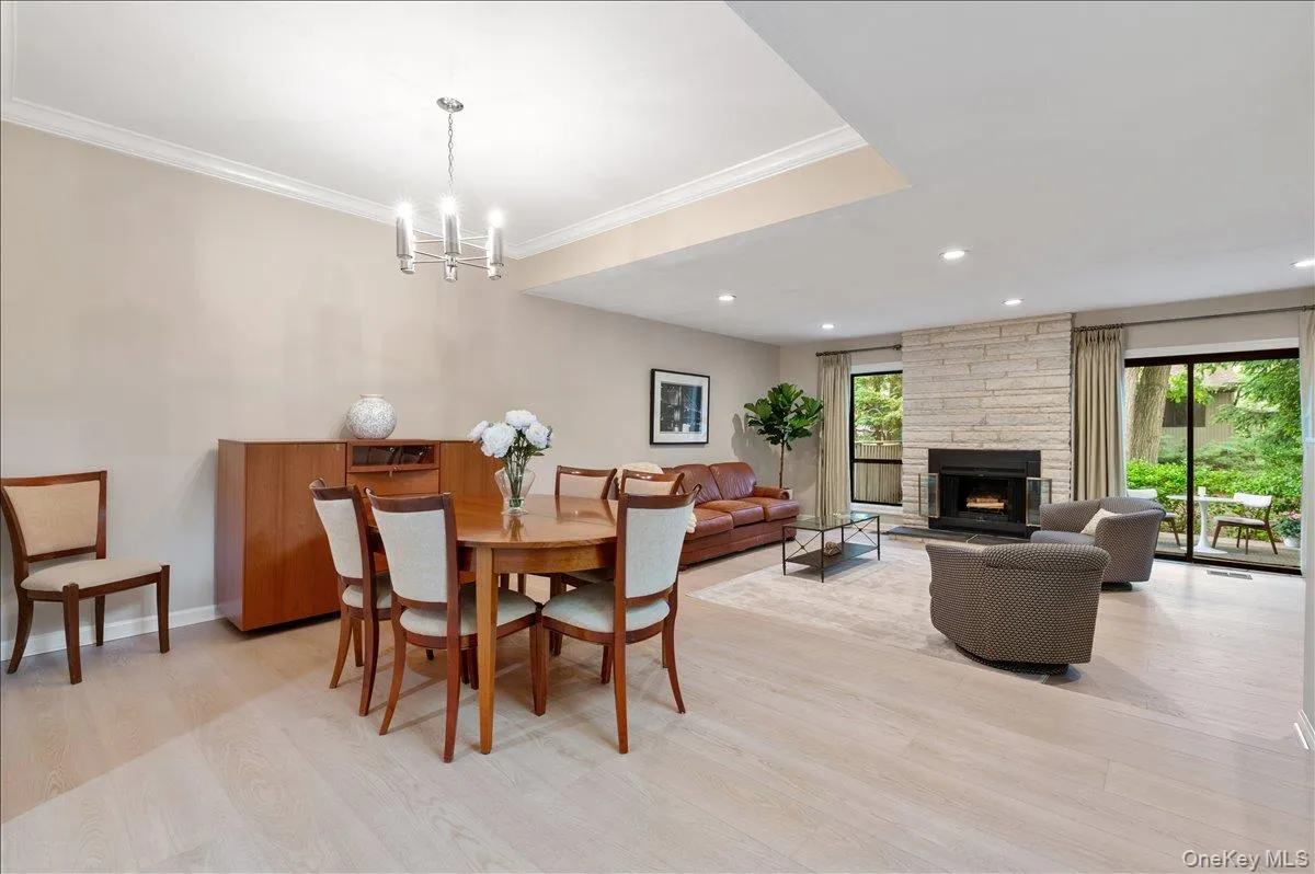 Spacious living & dining area featuring light wood-finish flooring, a stone-faced fireplace, recessed lighting, and crown molding Spacious living & dining area featuring light wood-finish flooring, a stone-faced fireplace, recessed lighting, and crown molding