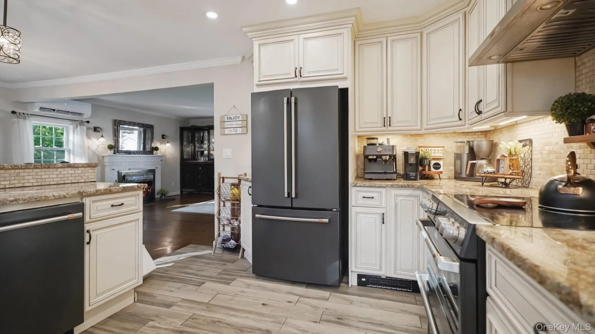 Kitchen featuring light-toned cabinetry, wood-finish flooring, a black-finish refrigerator, and a built-in range with an overhead exhaust fan Kitchen featuring light-toned cabinetry, wood-finish flooring, a black-finish refrigerator, and a built-in range with an overhead exhaust fan